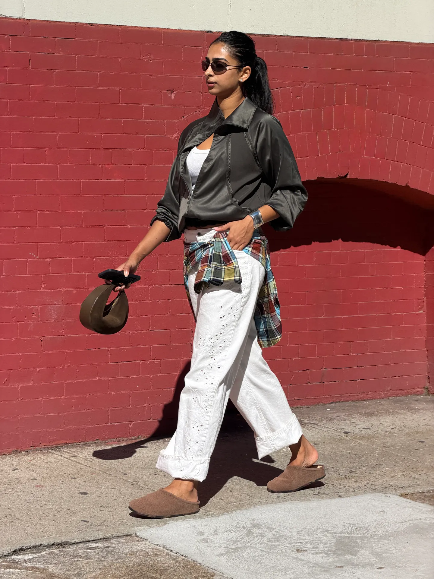 Dark green satin bomber, white embroidered wide-leg pants, plaid shirt, brown mules, and sunglasses.