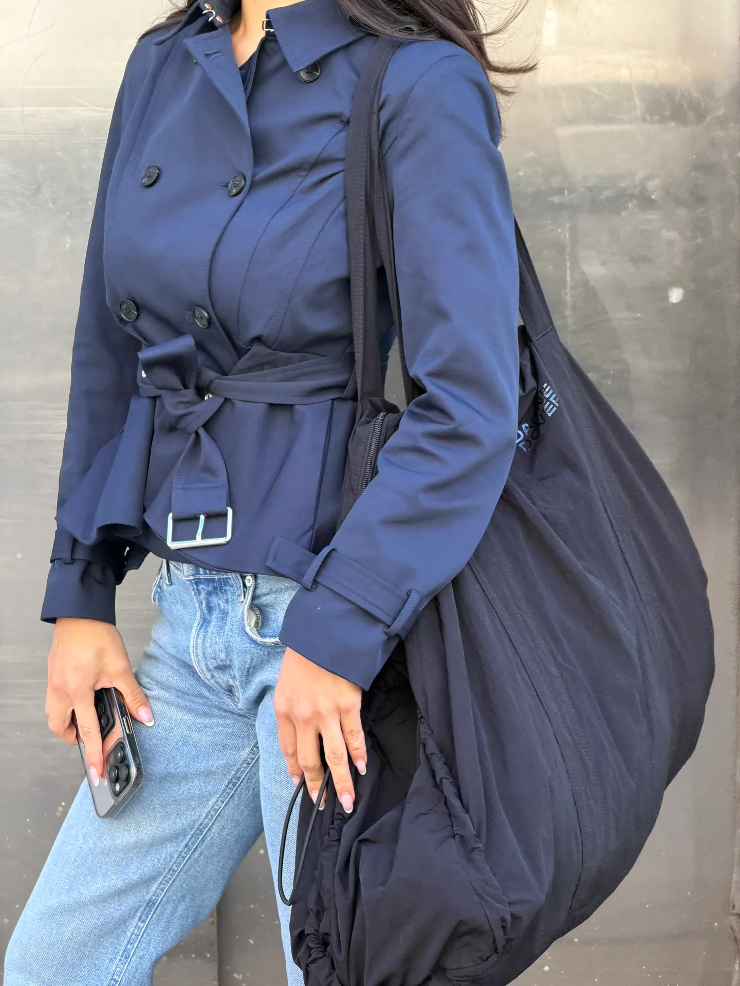 Navy belted trench jacket, light wash jeans, and an oversized black tote bag.
