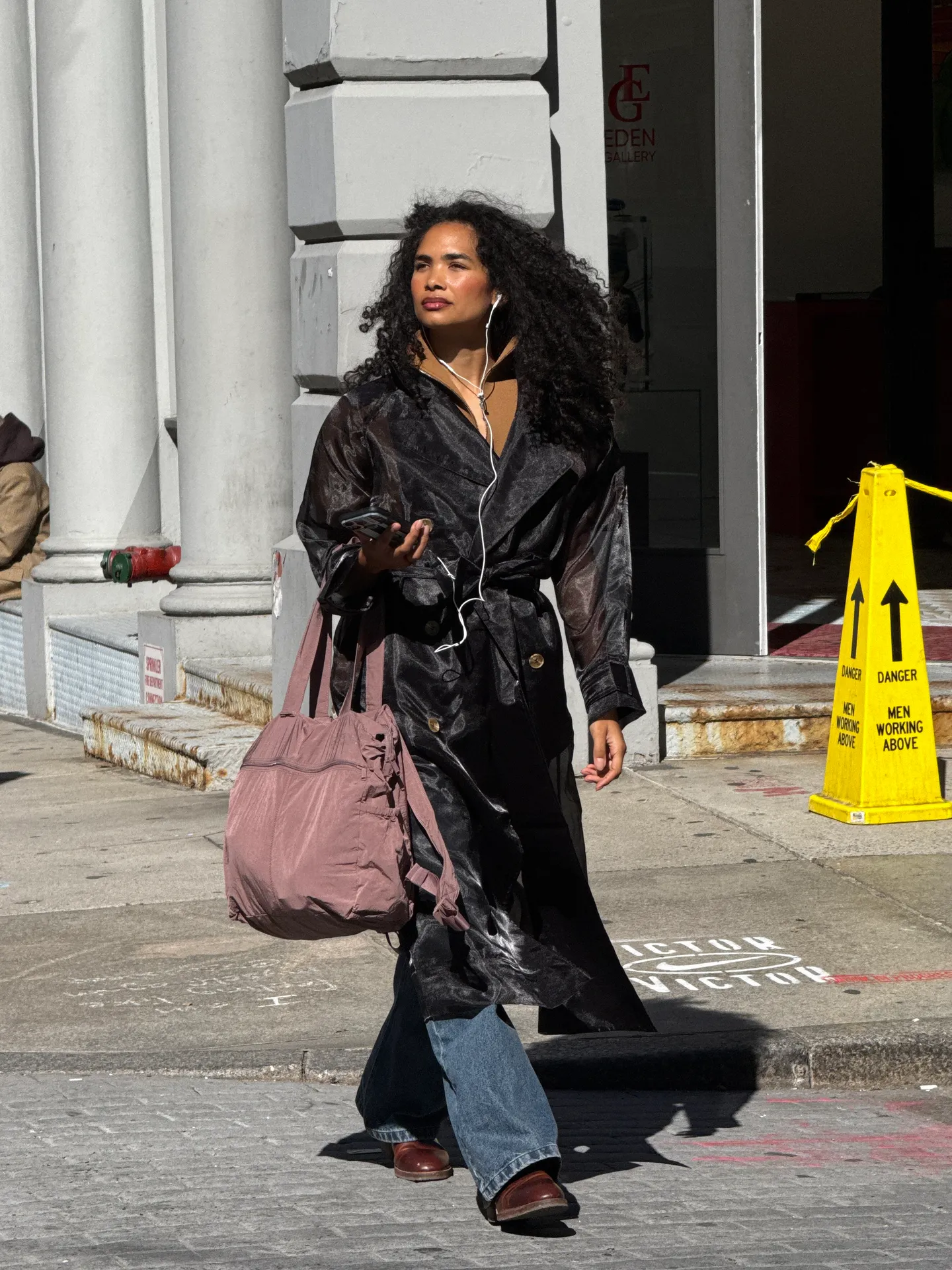 Sheer black trench coat, blue jeans, brown shoes, and a large dusty pink tote bag.