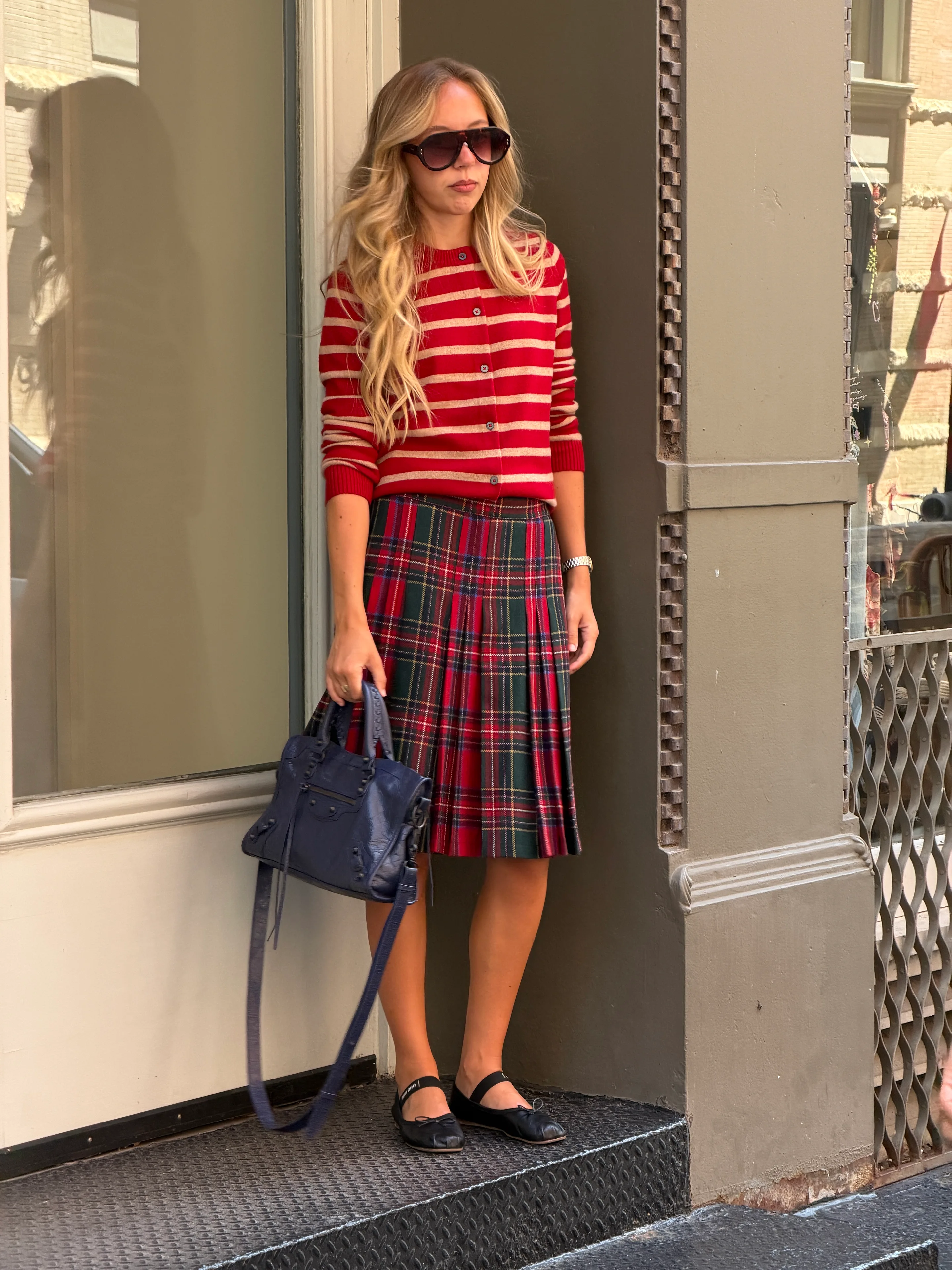 Red striped cardigan, plaid midi skirt, black ballet flats, and a navy handbag.