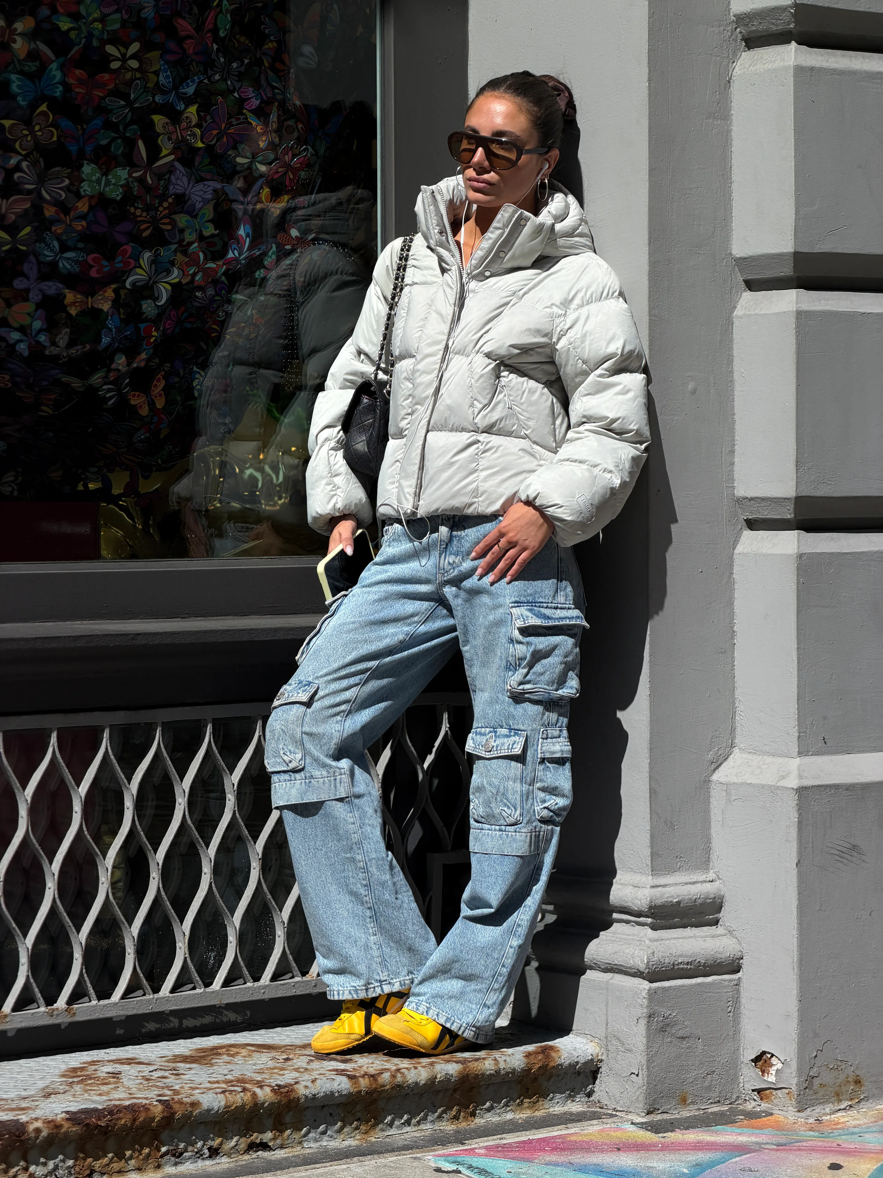 Light grey puffer jacket, light wash baggy cargo jeans, yellow sneakers, black quilted bag.
