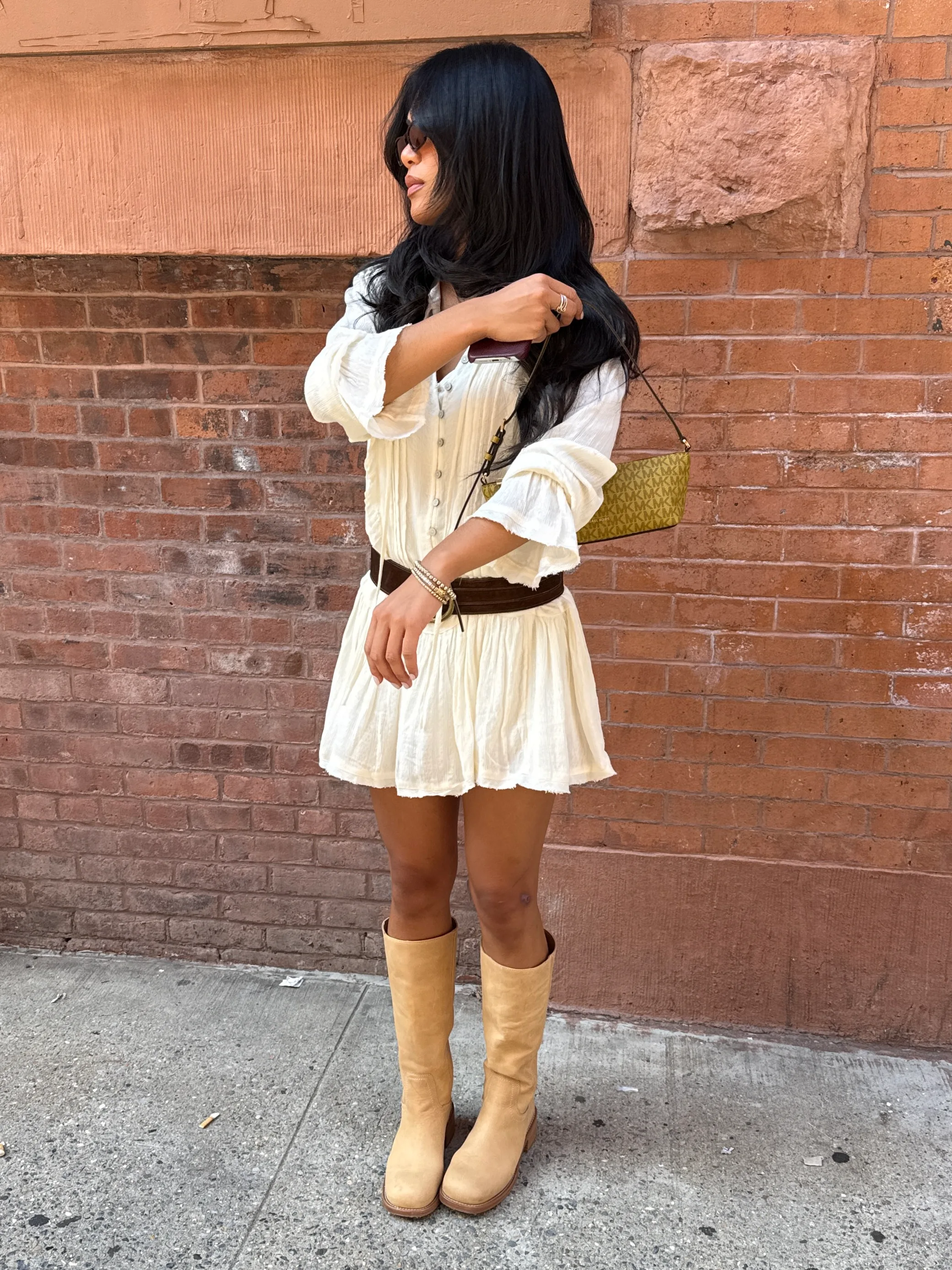 White mini dress with brown belt, tan boots, and a green patterned shoulder bag.