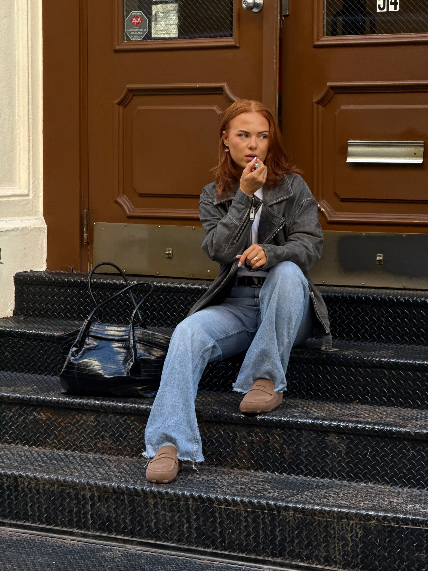 Distressed gray leather jacket, light wash flared jeans, and brown loafers on black stairs.