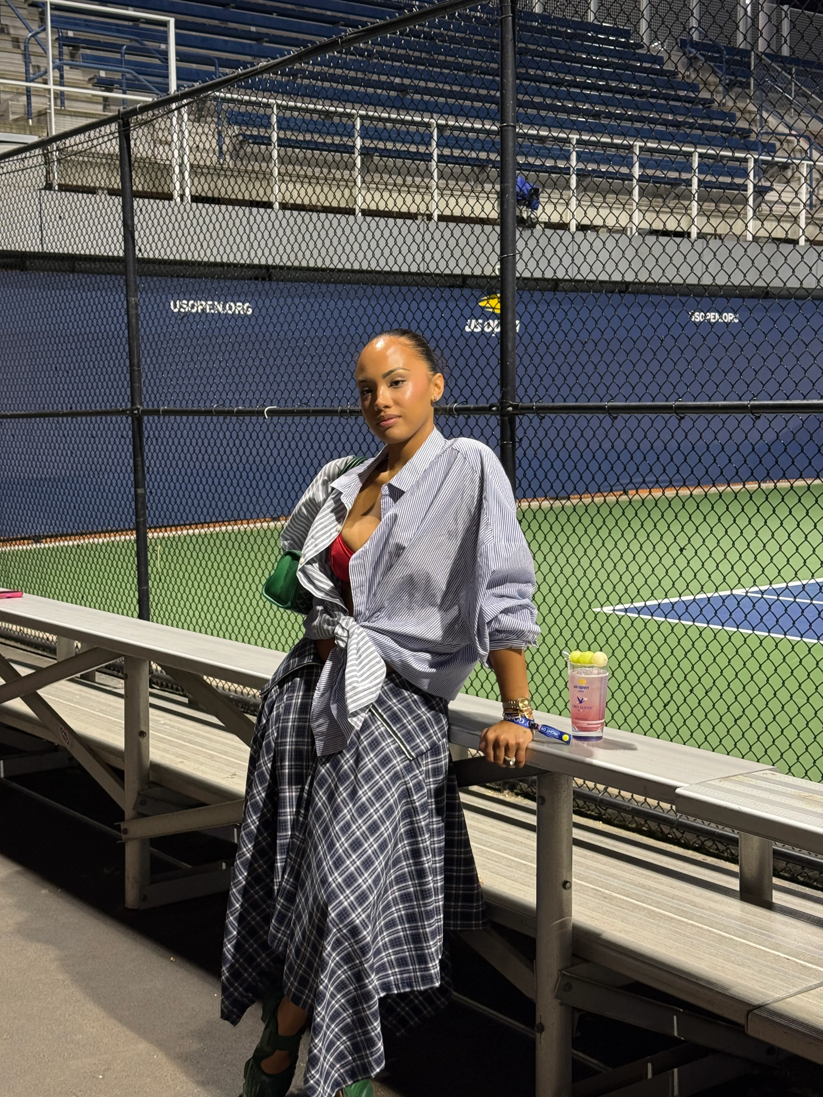 Blue and white striped shirt, red bra, and plaid midi skirt at a tennis court.