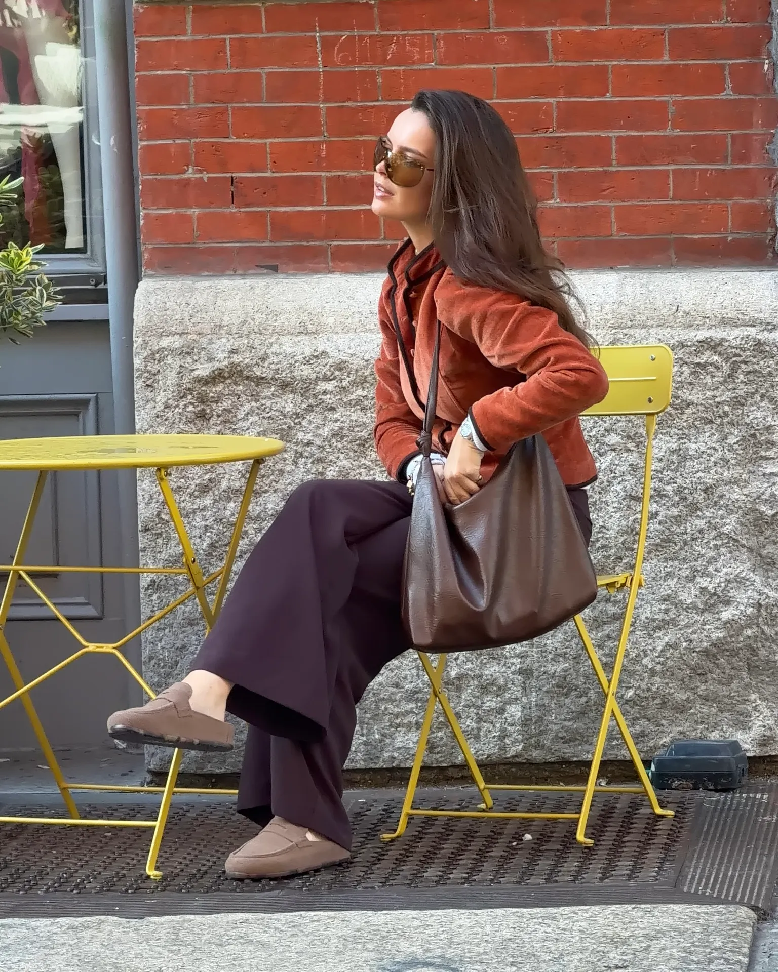 Orange velvet jacket, wide-leg brown pants, tan loafers, brown shoulder bag.