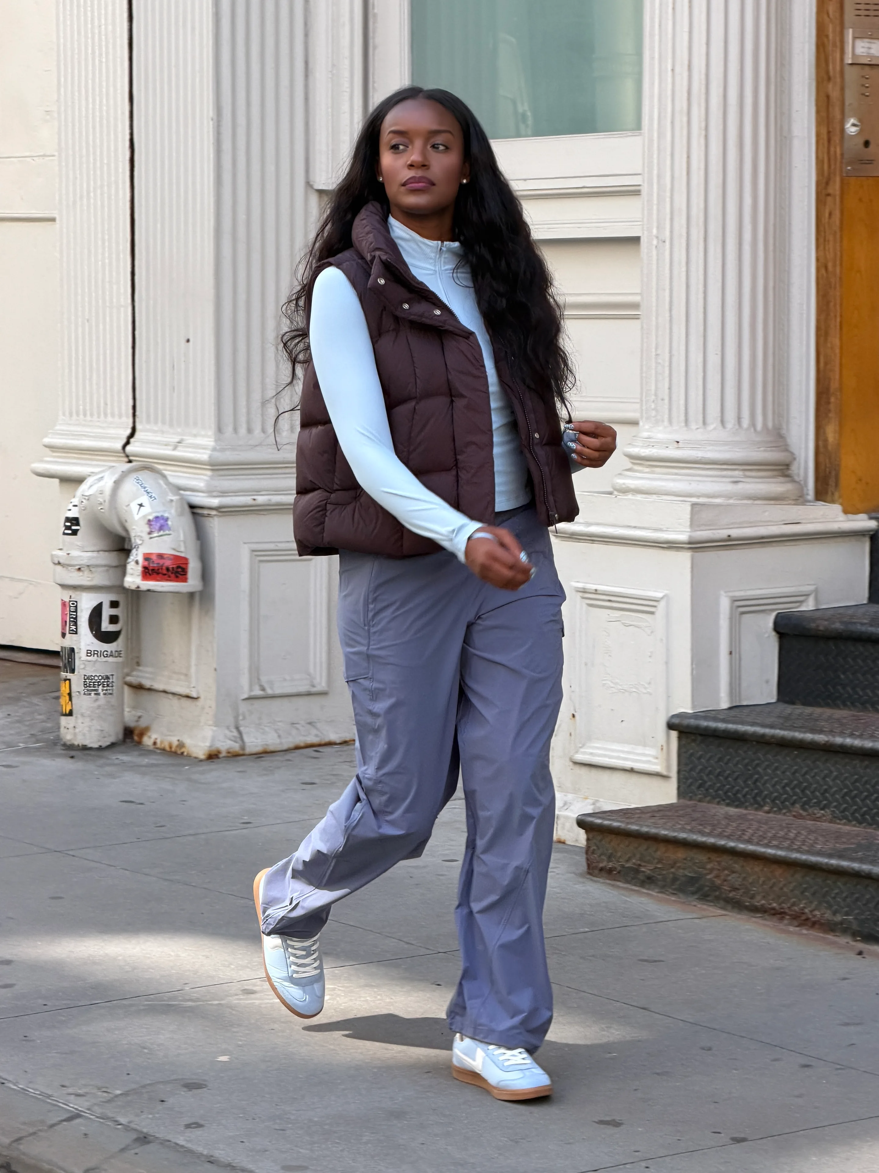 Brown quilted vest over a light blue top, gray track pants, and blue sneakers.