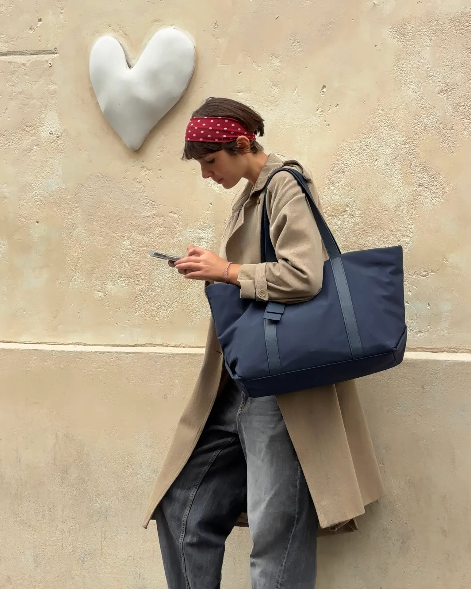 Red polka dot bandana, beige trench coat, and baggy jeans with a navy tote bag.