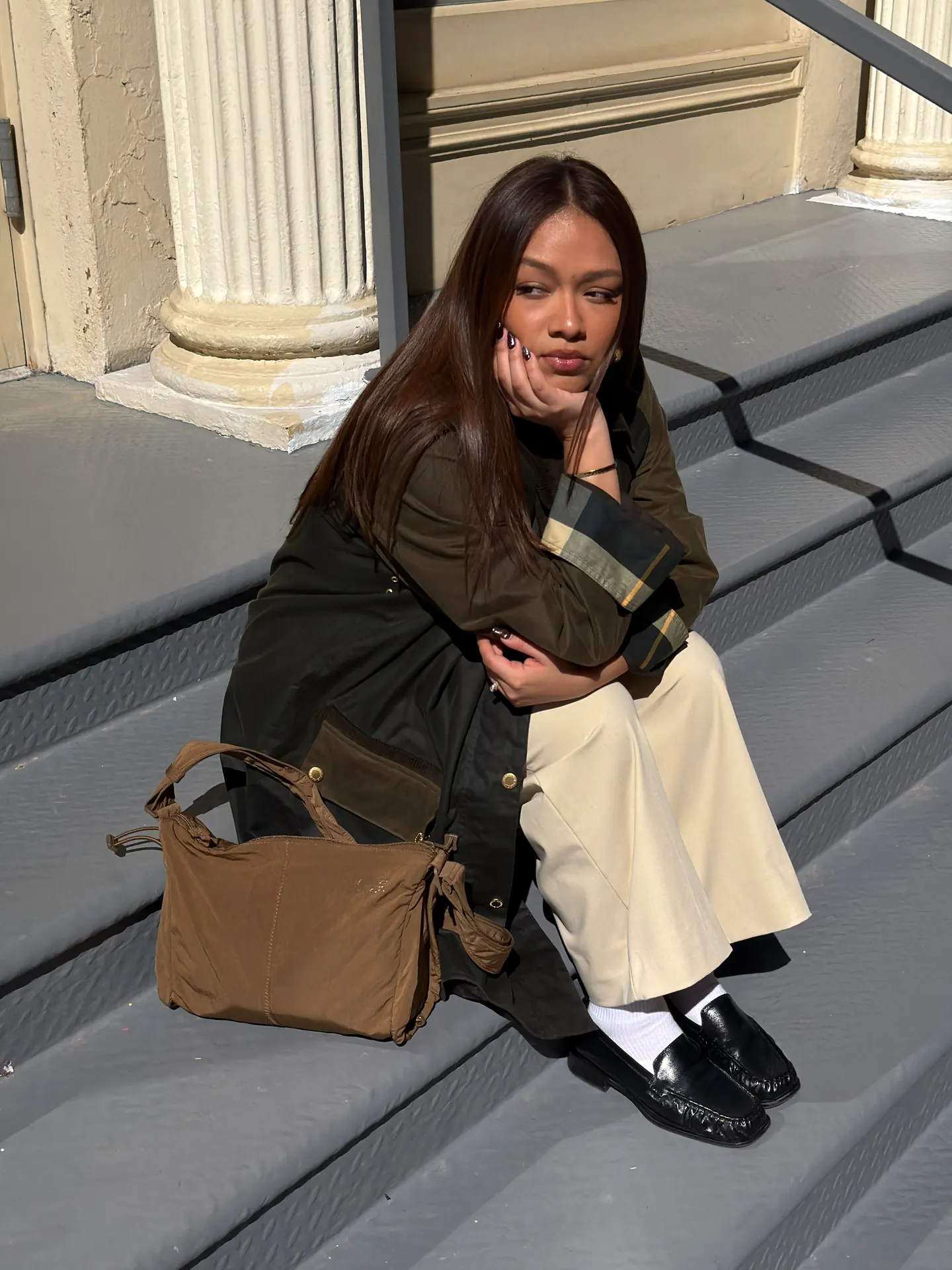 Dark green coat with plaid cuffs, cream wide-leg pants, black loafers, and a brown bag.