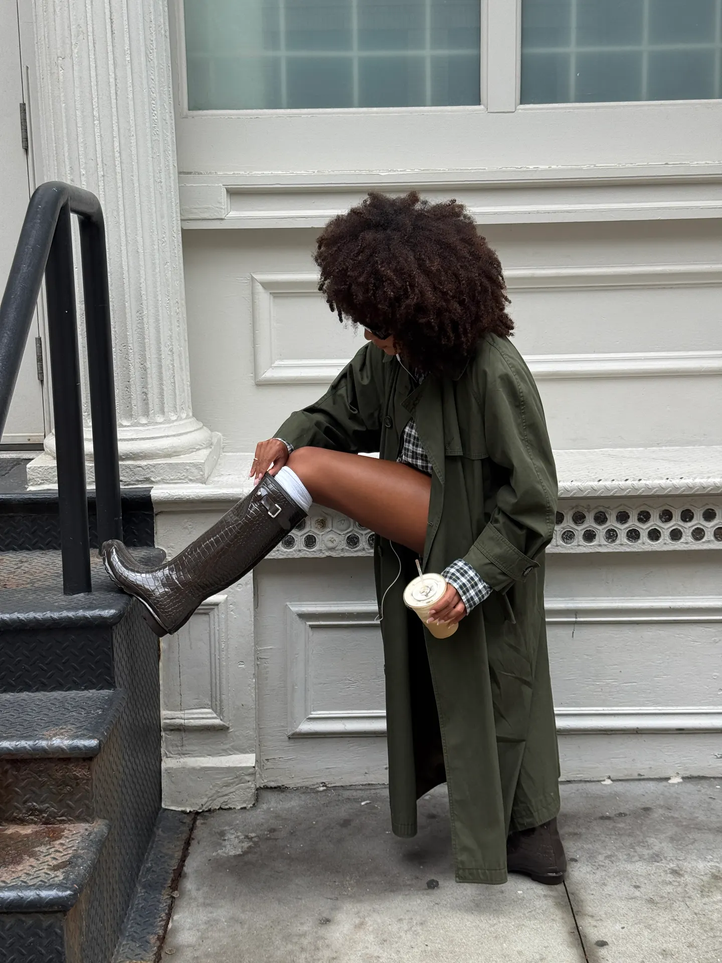 Olive green trench coat, plaid top, and crocodile-embossed rain boots street style.
