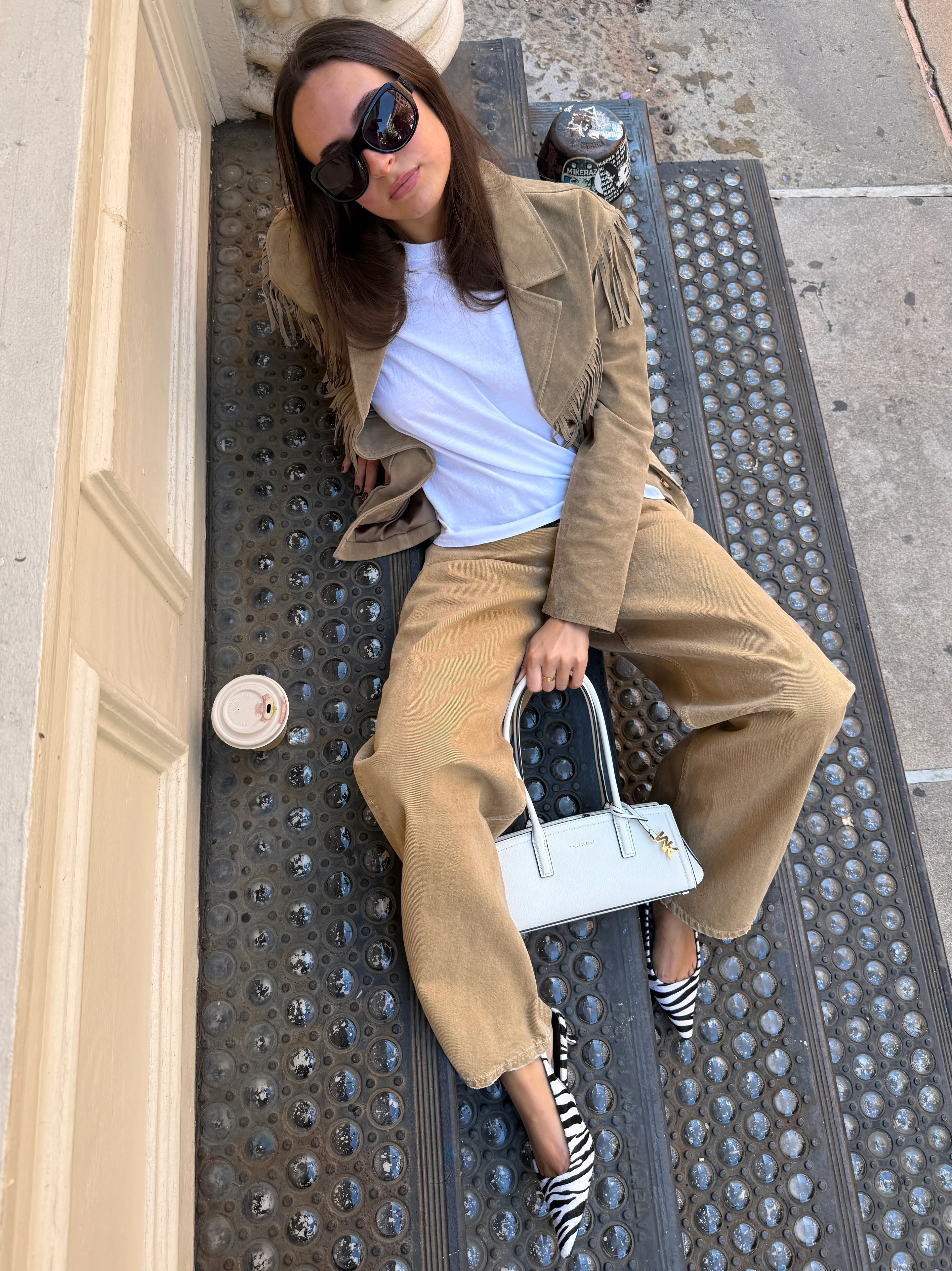 Brown fringe suede jacket, white t-shirt, tan pants, zebra print heels, and white shoulder bag.
