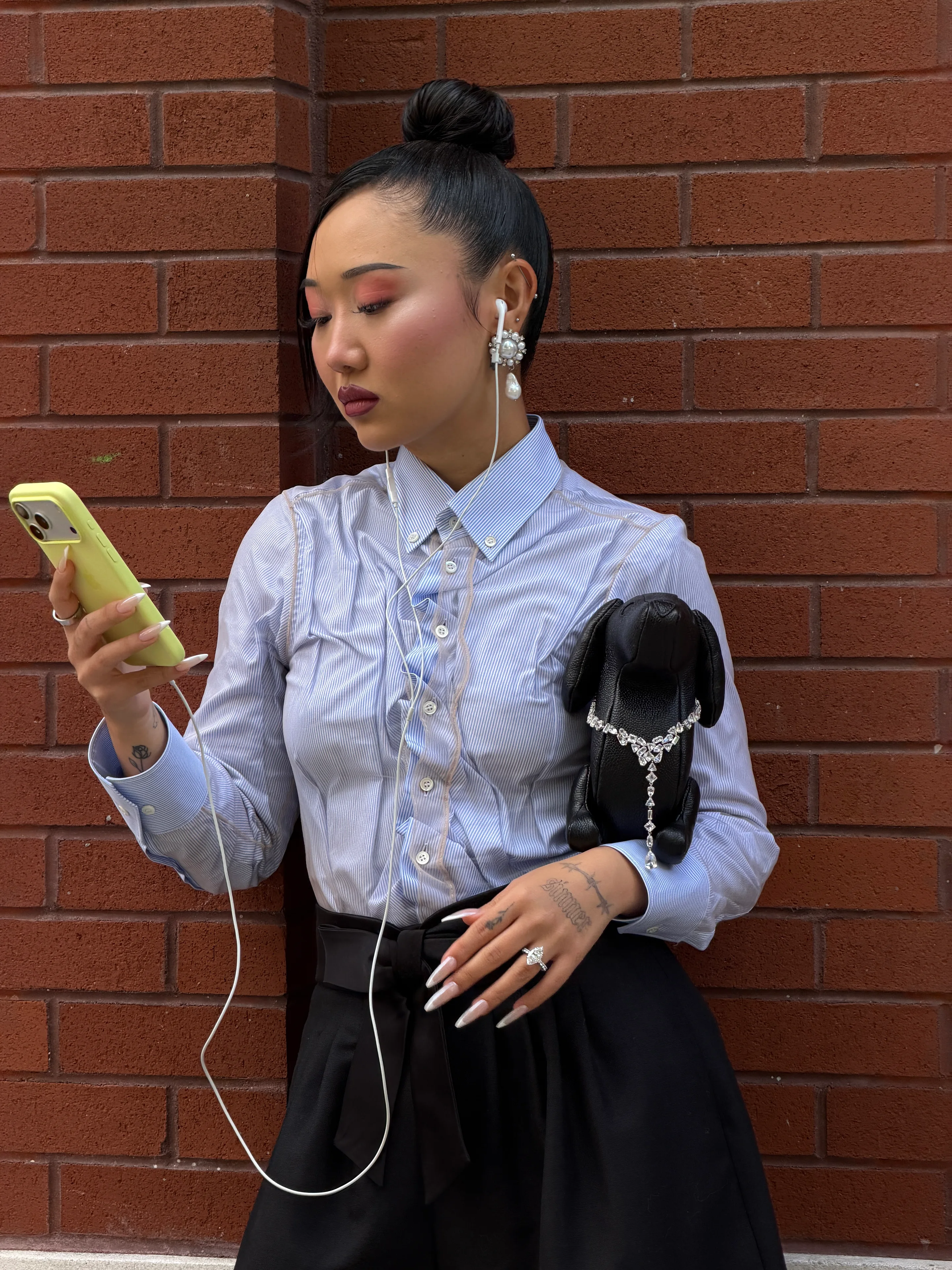 Blue pinstripe button-down shirt with a black skirt, pearl earrings, and a dog-shaped bag.