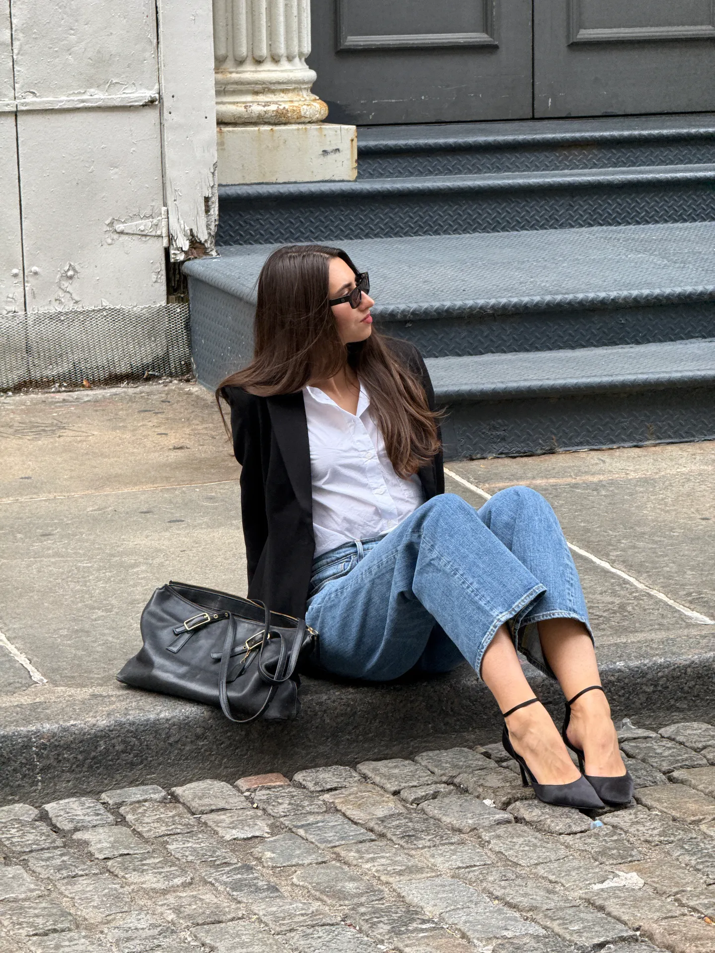 Black blazer over white shirt, wide-leg jeans, black ankle-strap heels, and black handbag.