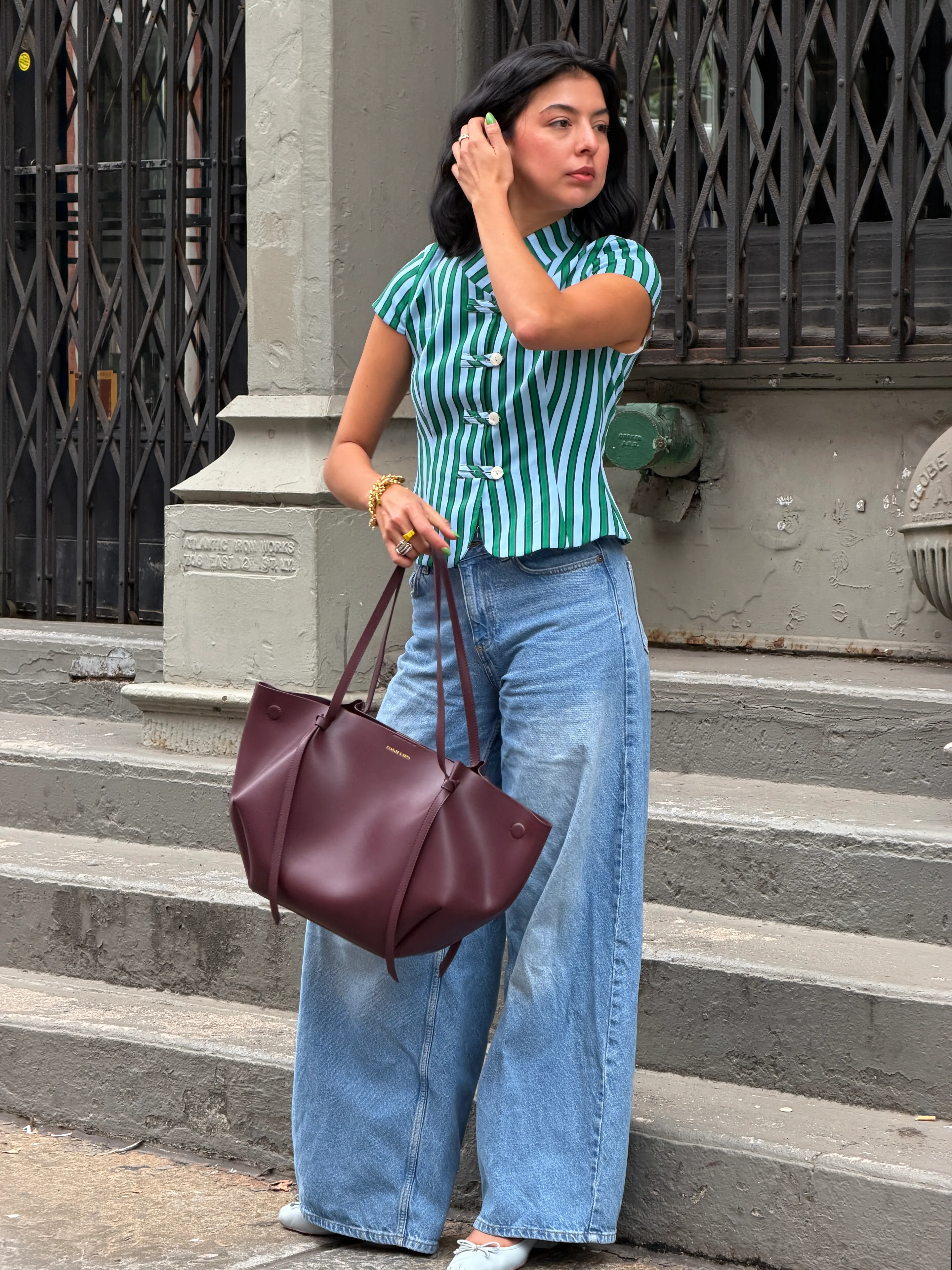 Green striped top, wide-leg jeans, and a burgundy tote bag.