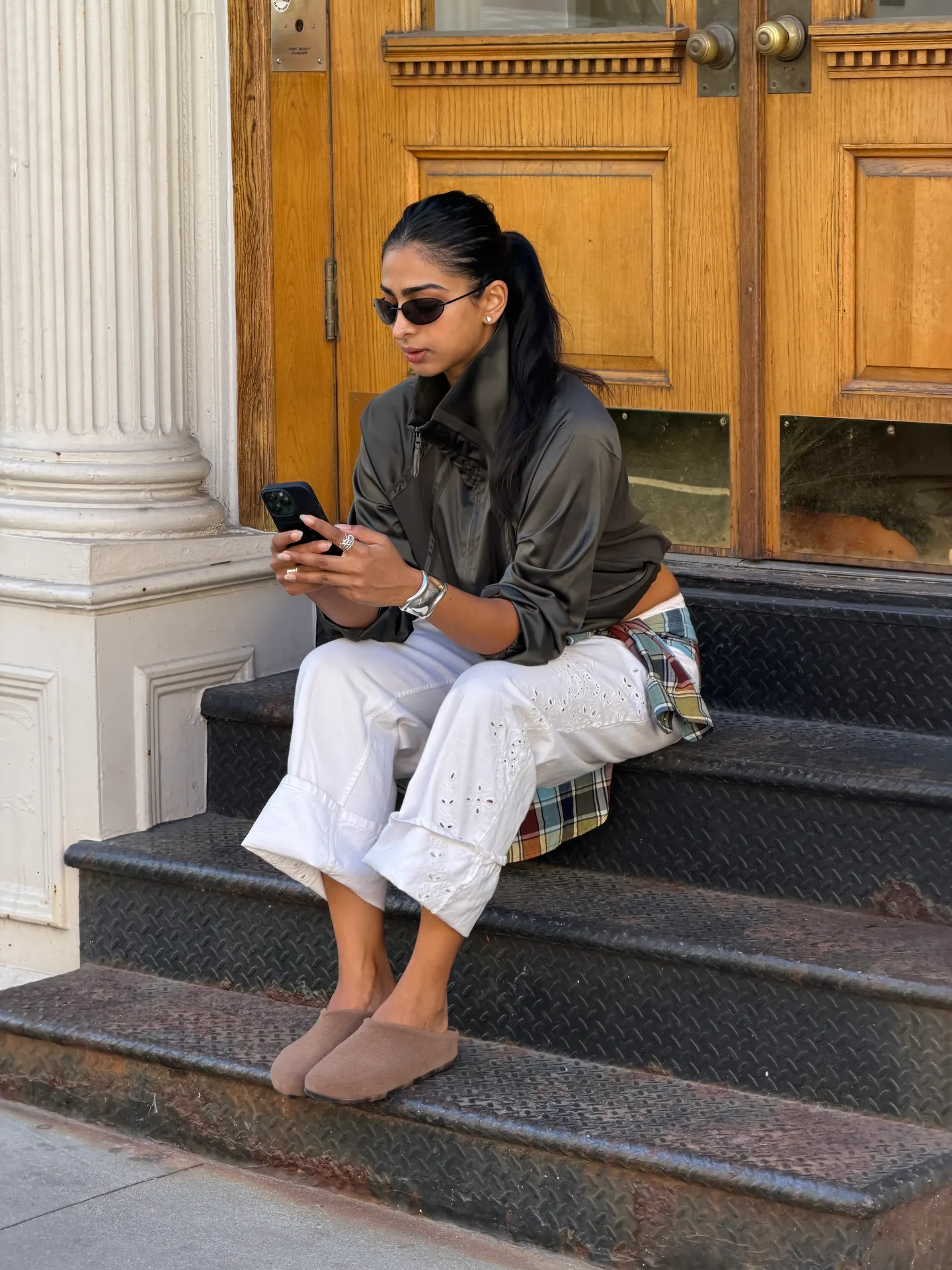 Gray high-neck jacket, white eyelet pants, brown mules, and plaid shirt tied at waist.