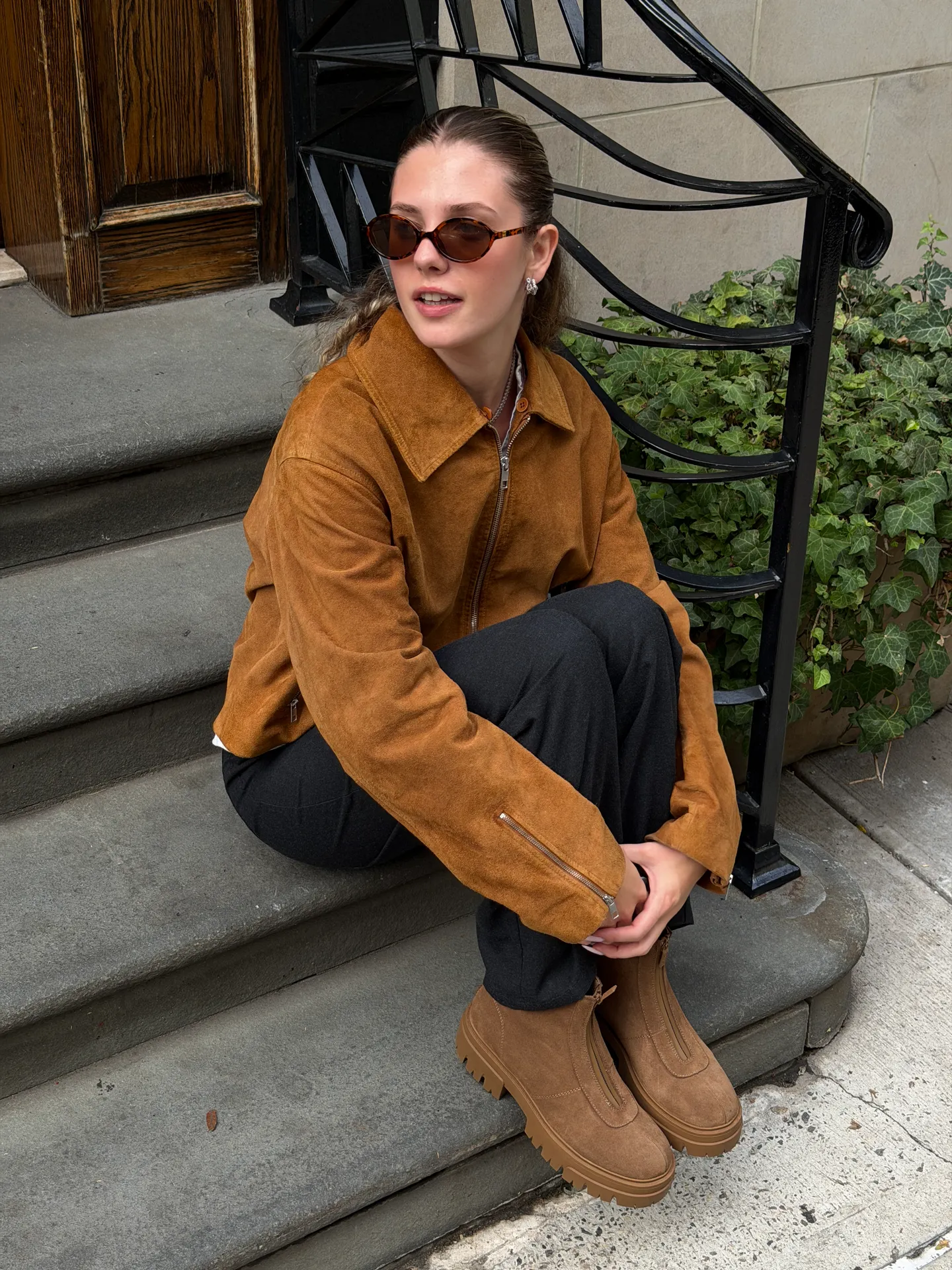 Brown suede jacket, black pants, brown lug-sole boots, and tortoise shell sunglasses.