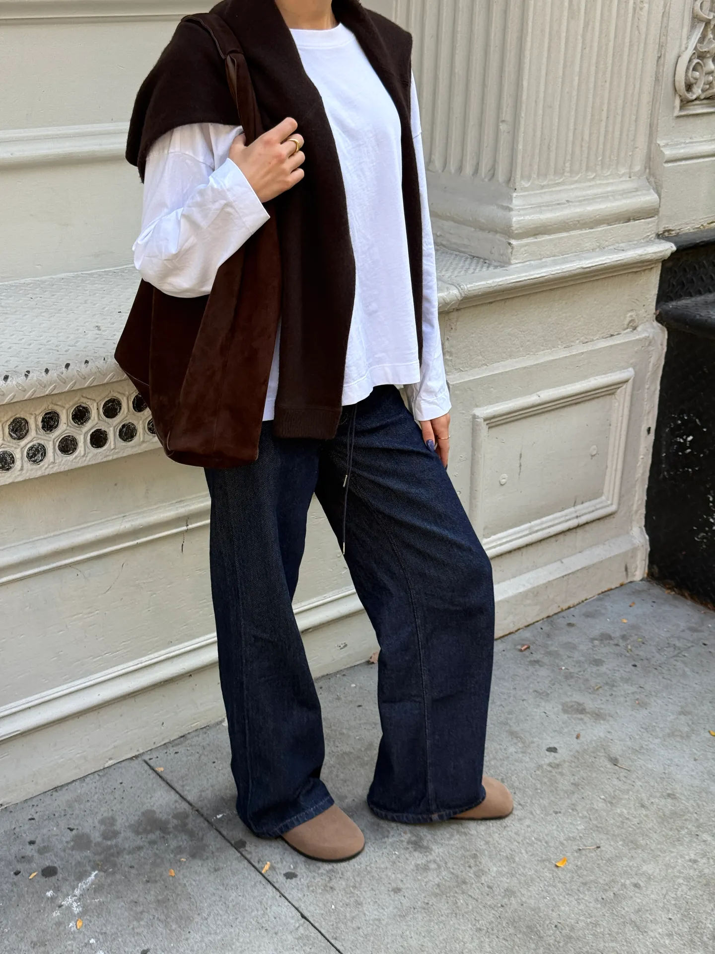 White long-sleeve top, dark wash wide-leg jeans, brown sweater, brown bag, and beige flats.
