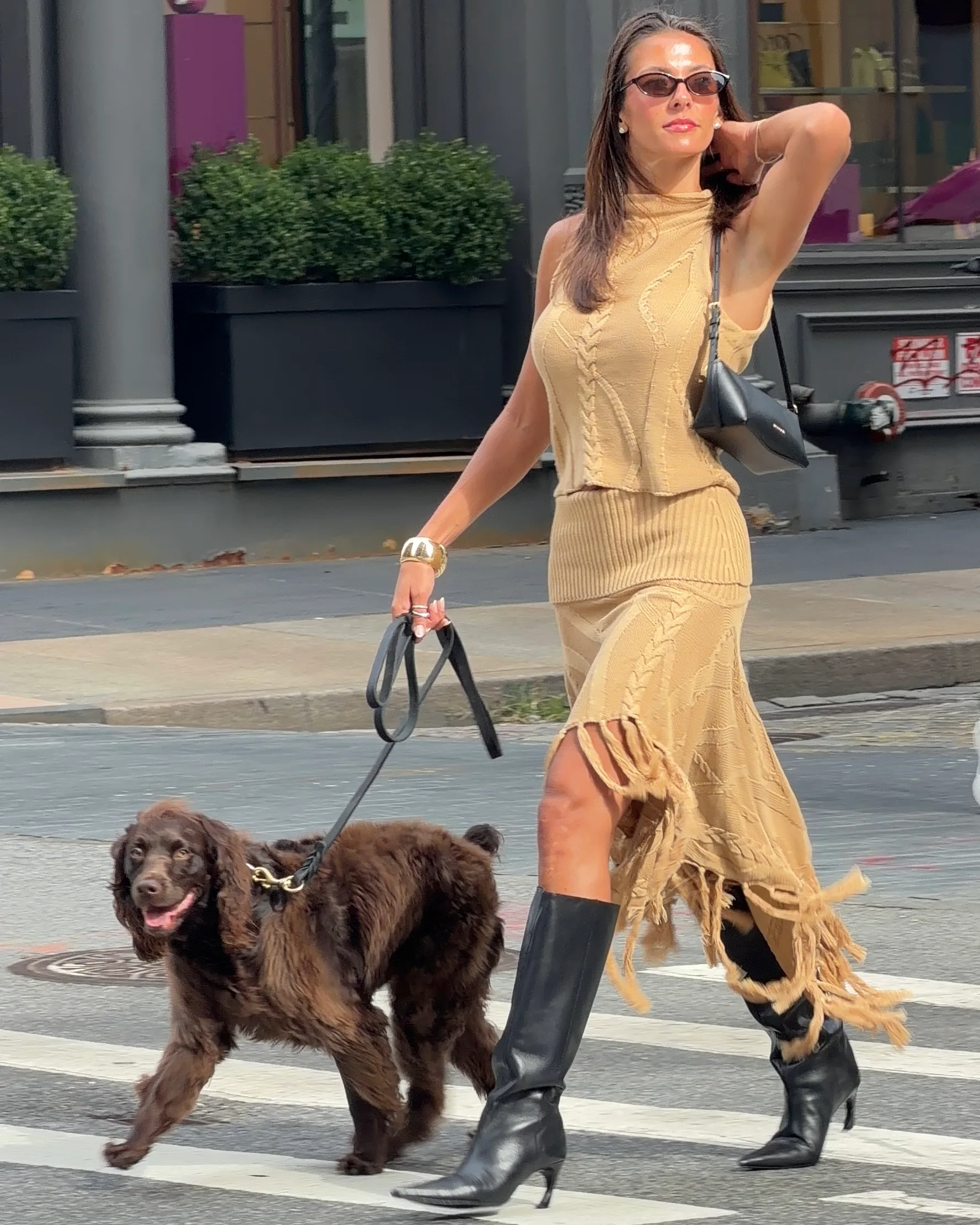 Beige knit top and fringe skirt, black boots, bag, and dog on city street.