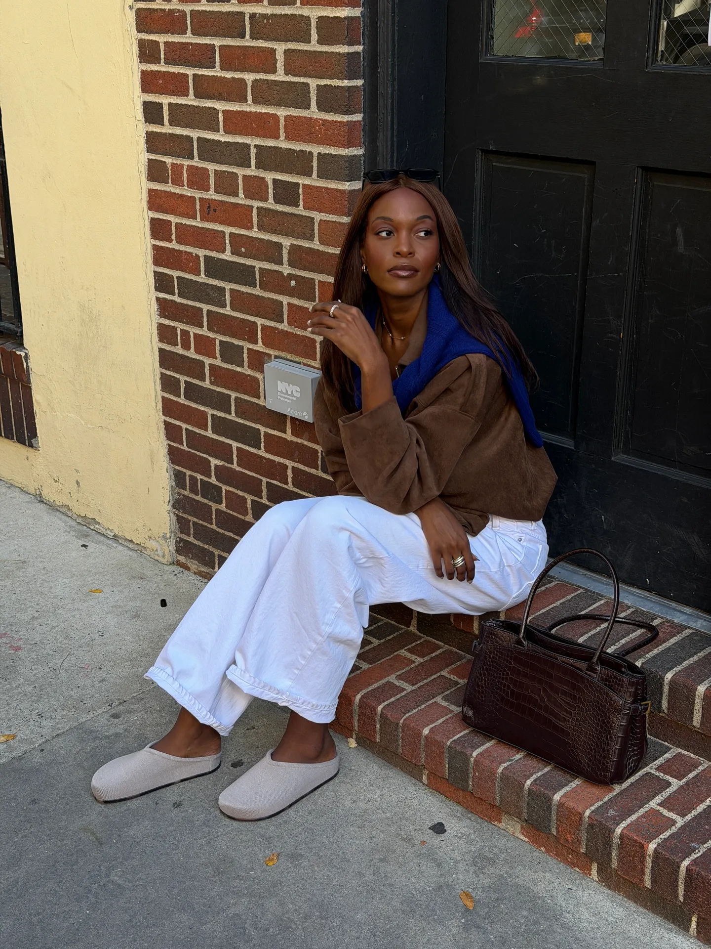 Brown suede shirt, blue sweater, white wide-leg pants, and grey mules.