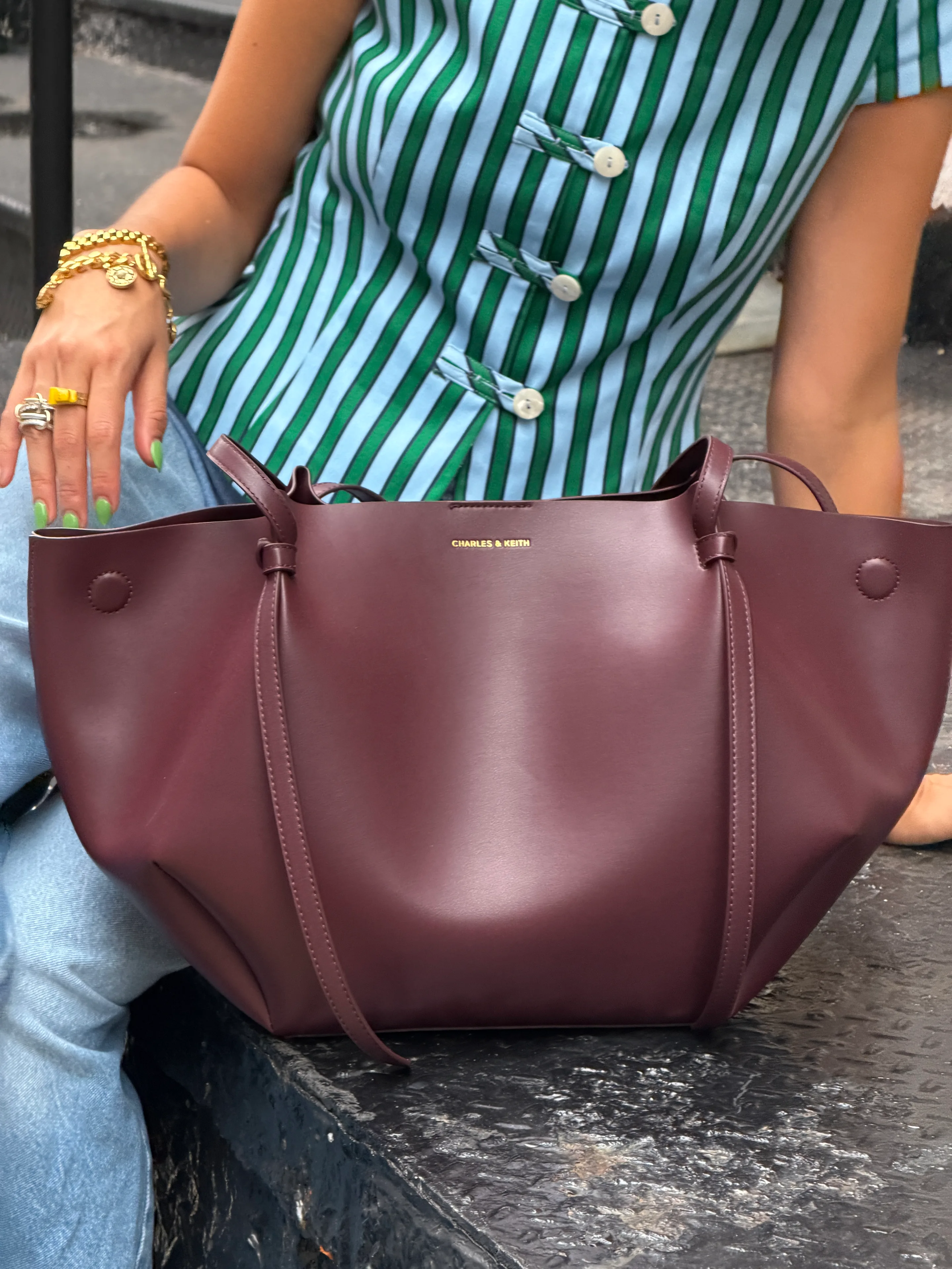 Green and blue striped top, light wash jeans, and a dark red CHARLES & KEITH tote bag.
