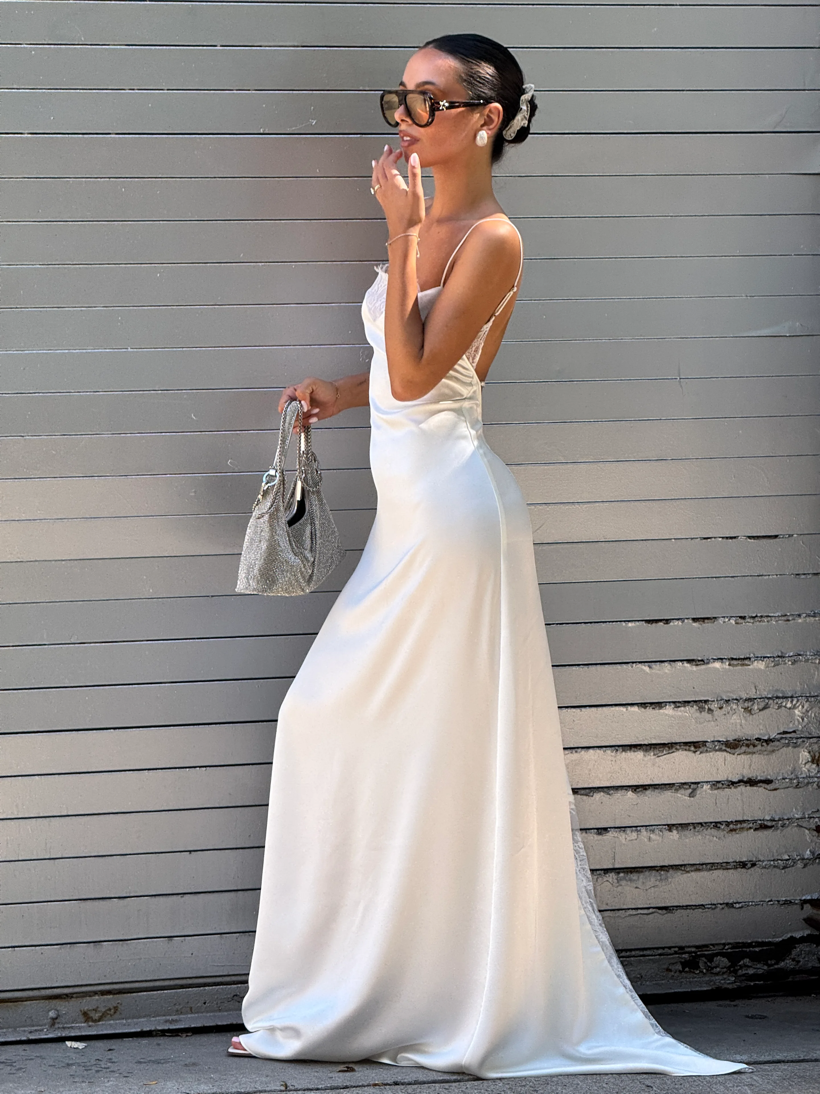 White satin slip dress with lace trim, tortoise sunglasses, and a sparkling silver handbag.