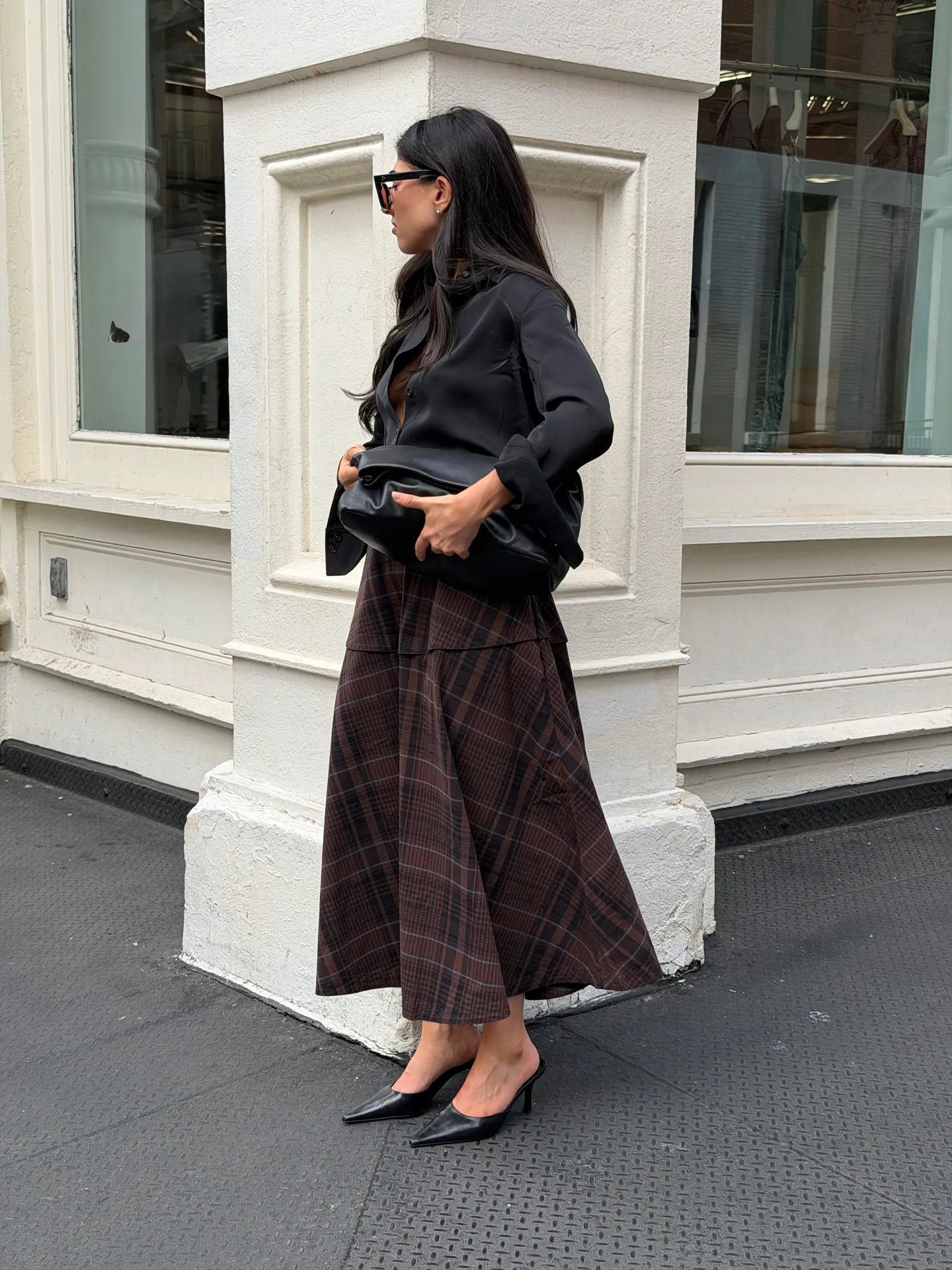 Black button-up shirt, brown plaid midi skirt, black mules, and black clutch.