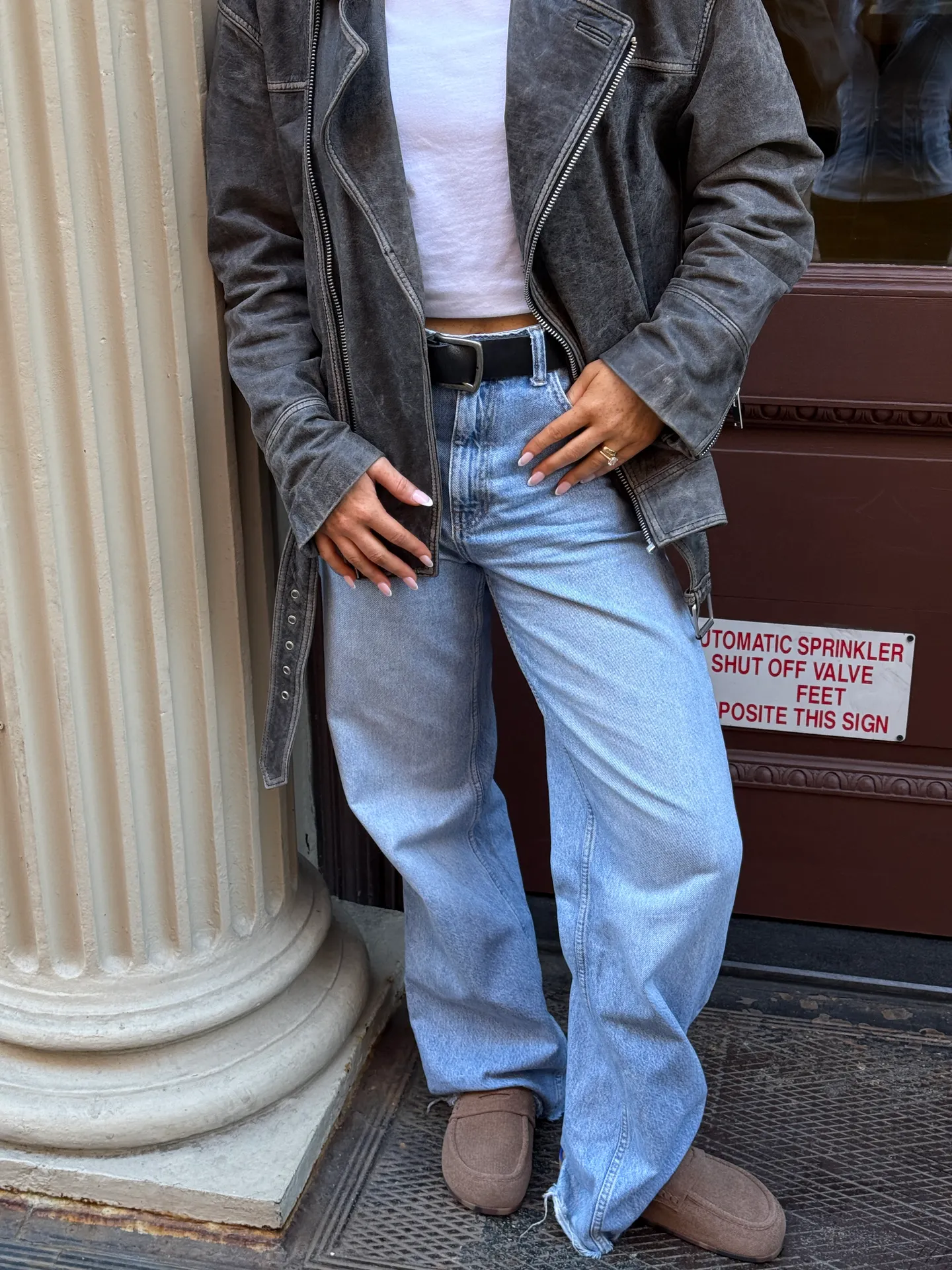 Washed black biker jacket, white crop top, light wash jeans, and brown loafers.