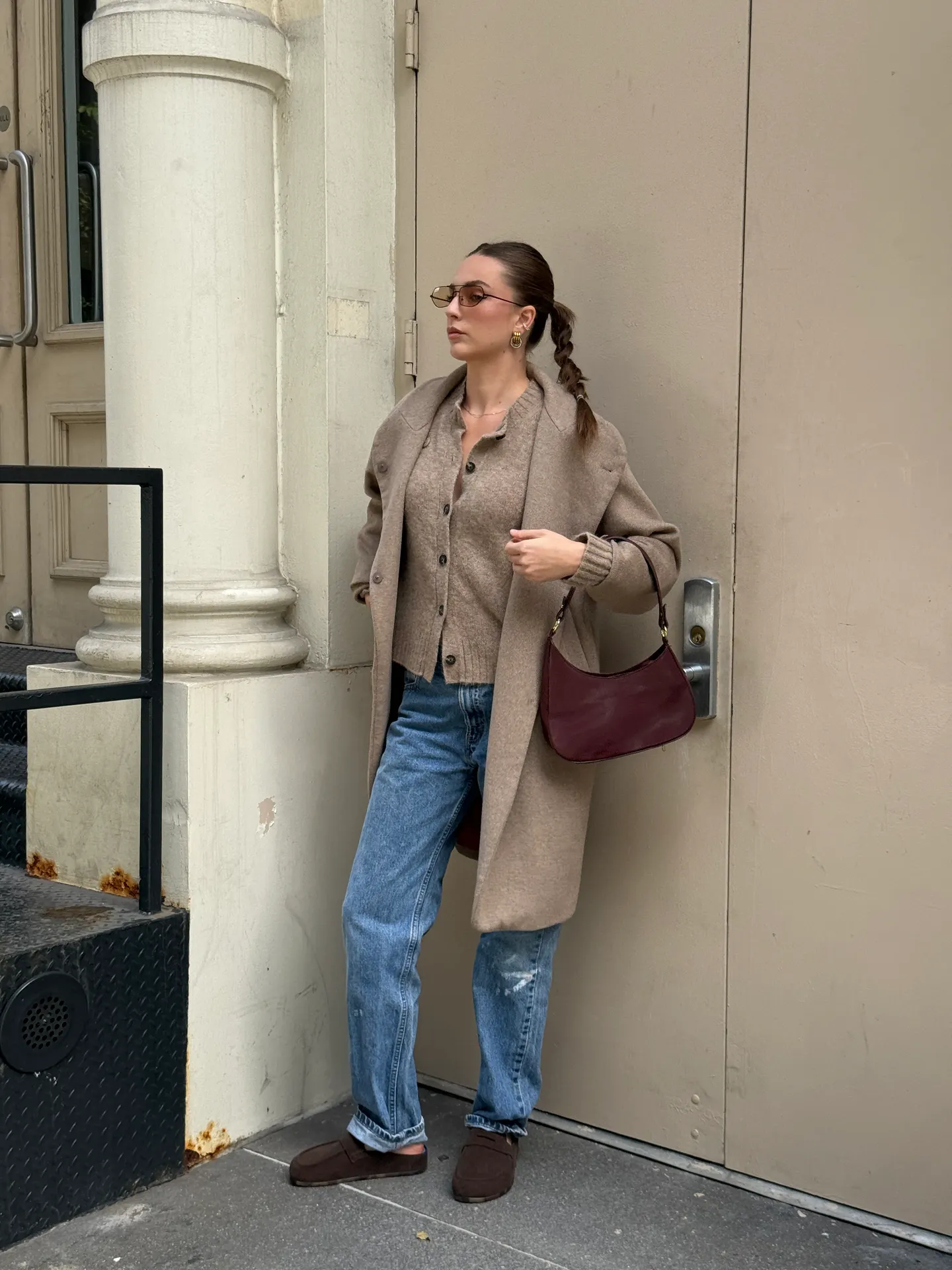 Tan coat, brown cardigan, distressed jeans, and maroon bag, with pigtails and sunglasses.