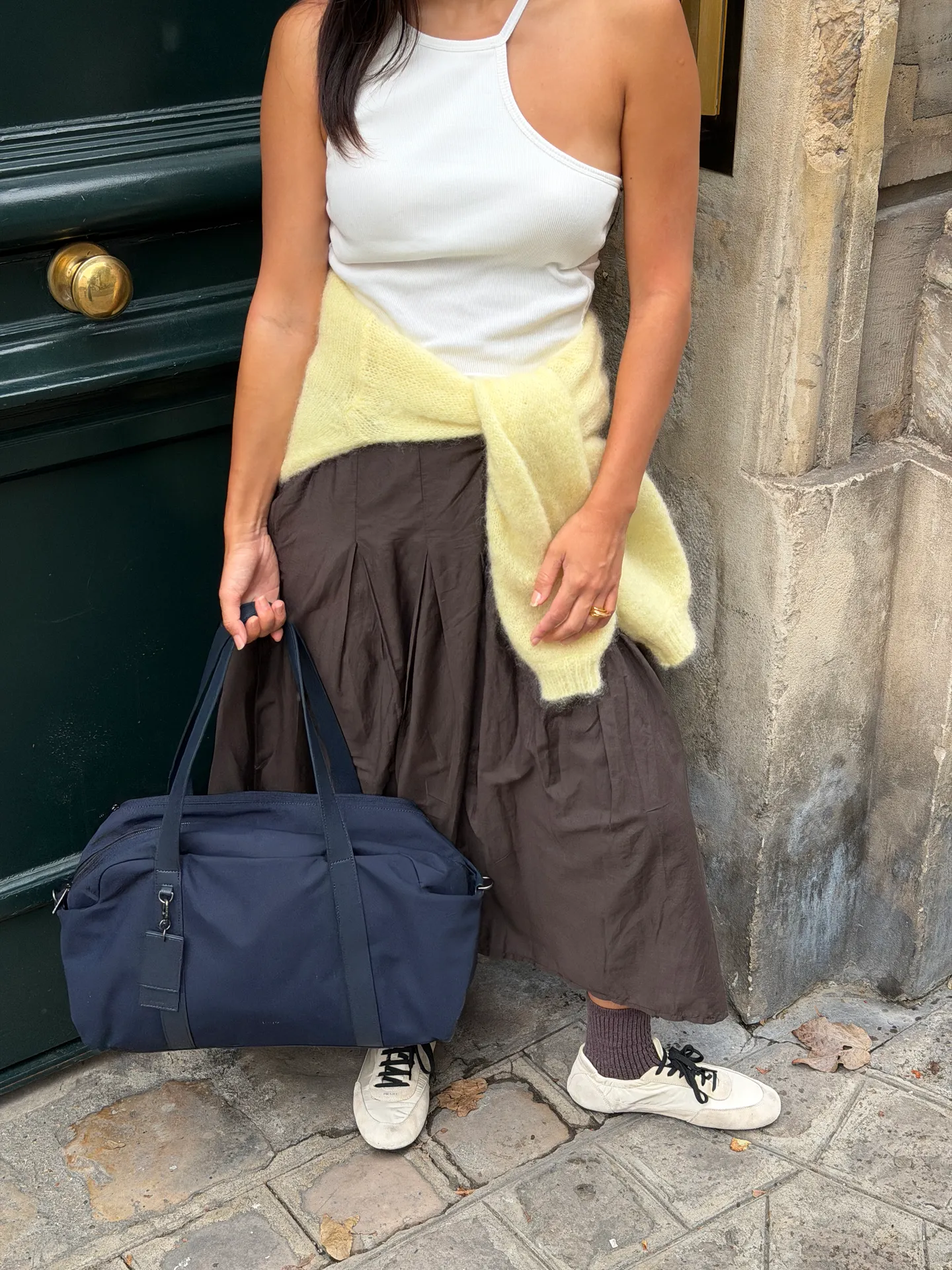 White halter top, brown midi skirt, yellow fuzzy sweater, white sneakers, and navy duffle bag.