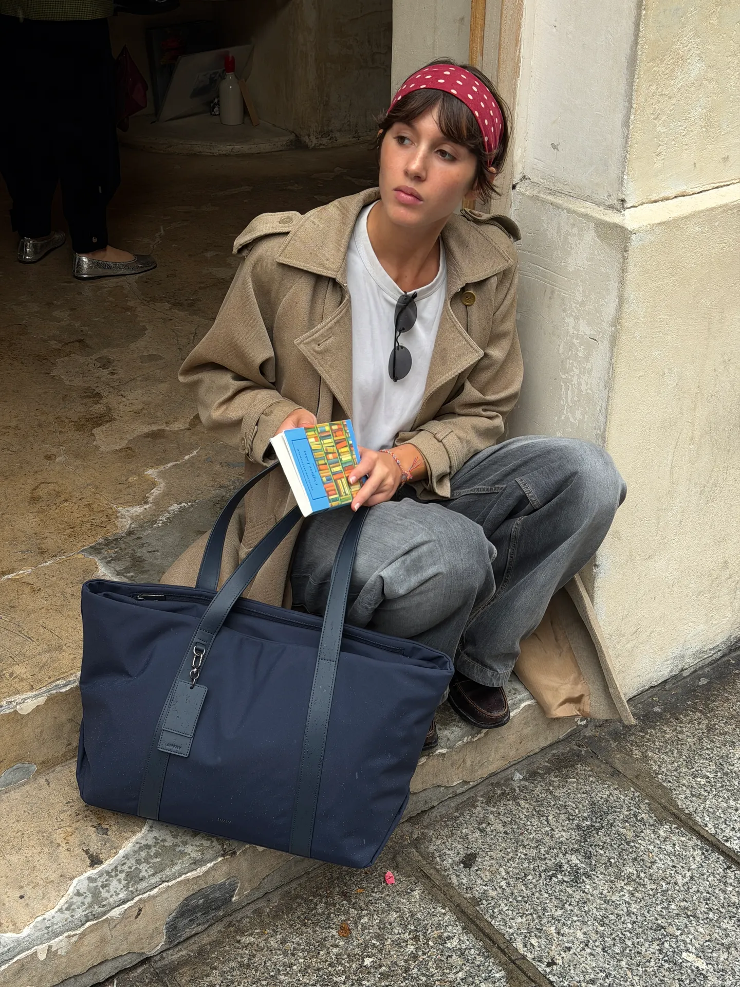 Khaki trench coat, white tee, grey jeans, red polka dot bandana, and navy tote bag.