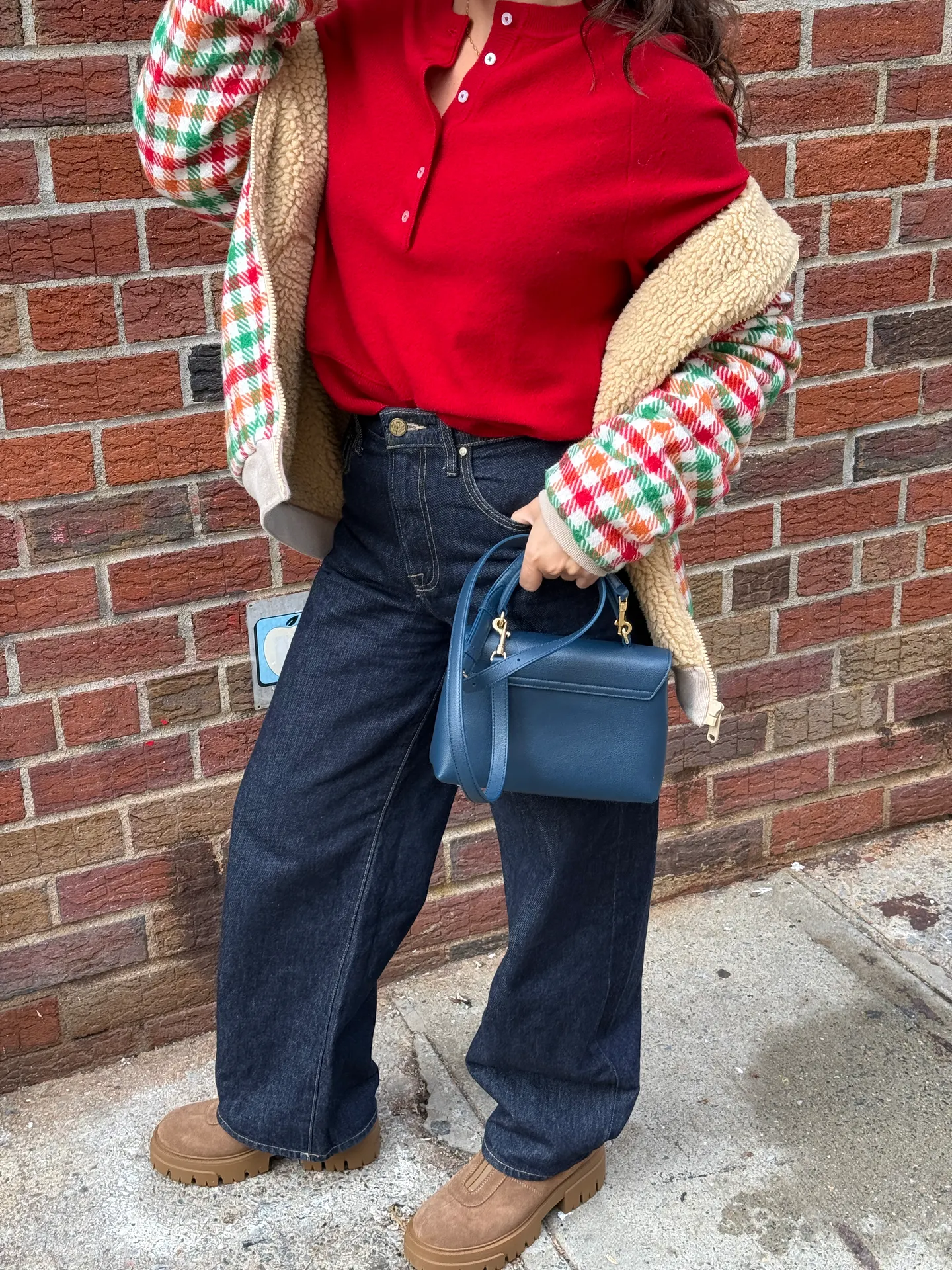 Red henley, dark wash jeans, plaid sherpa jacket, blue handbag, and brown lug sole boots.