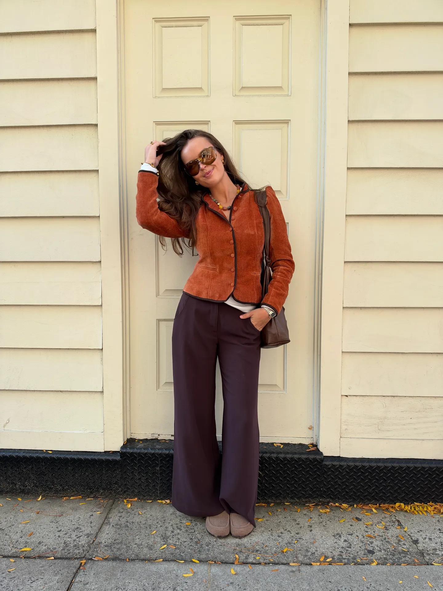 Rust suede jacket, wide-leg trousers, sunglasses, and beaded necklace.