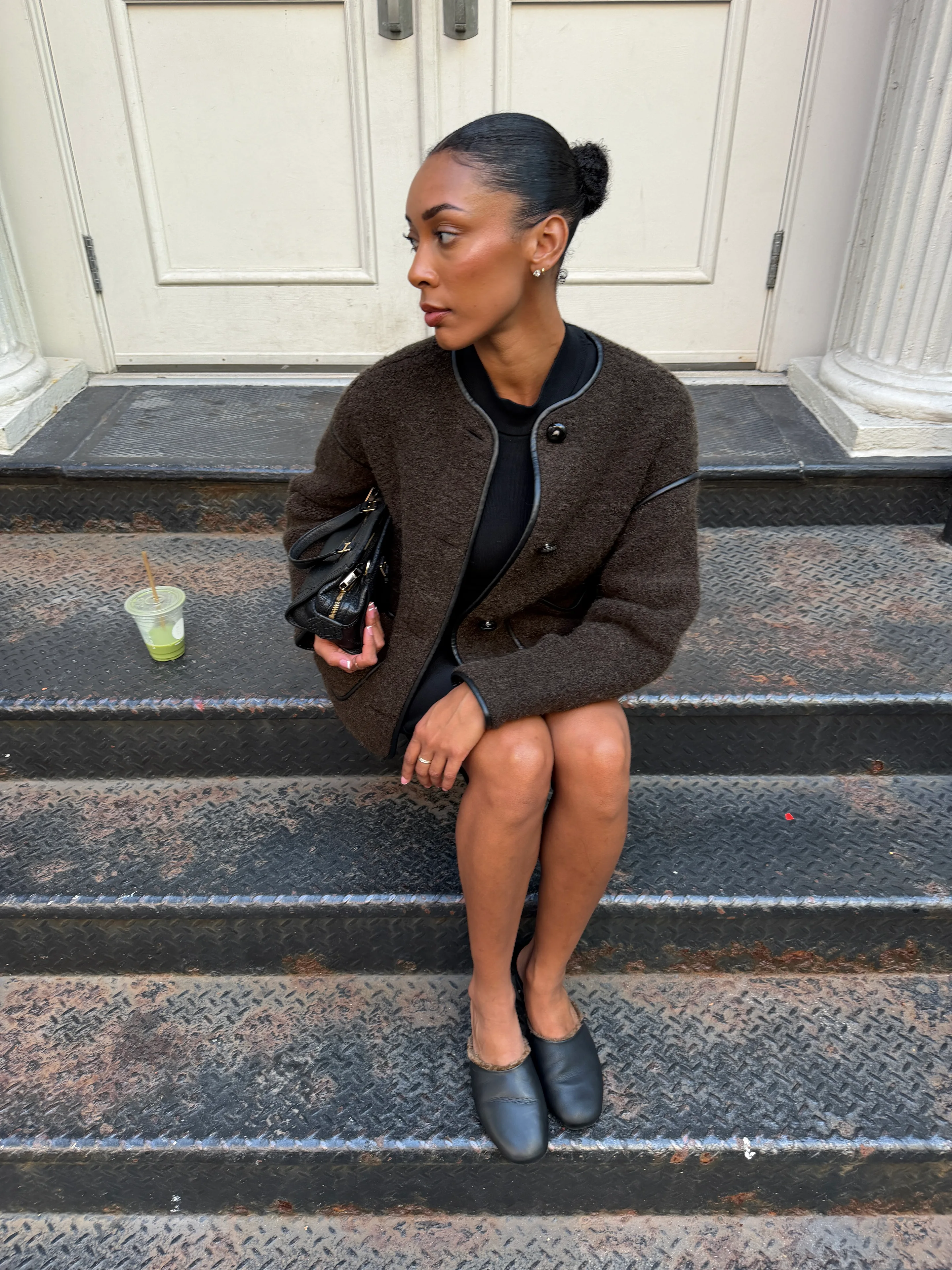 Dark brown boucle jacket with black trim, black dress, black fur-lined mules, and black handbag.