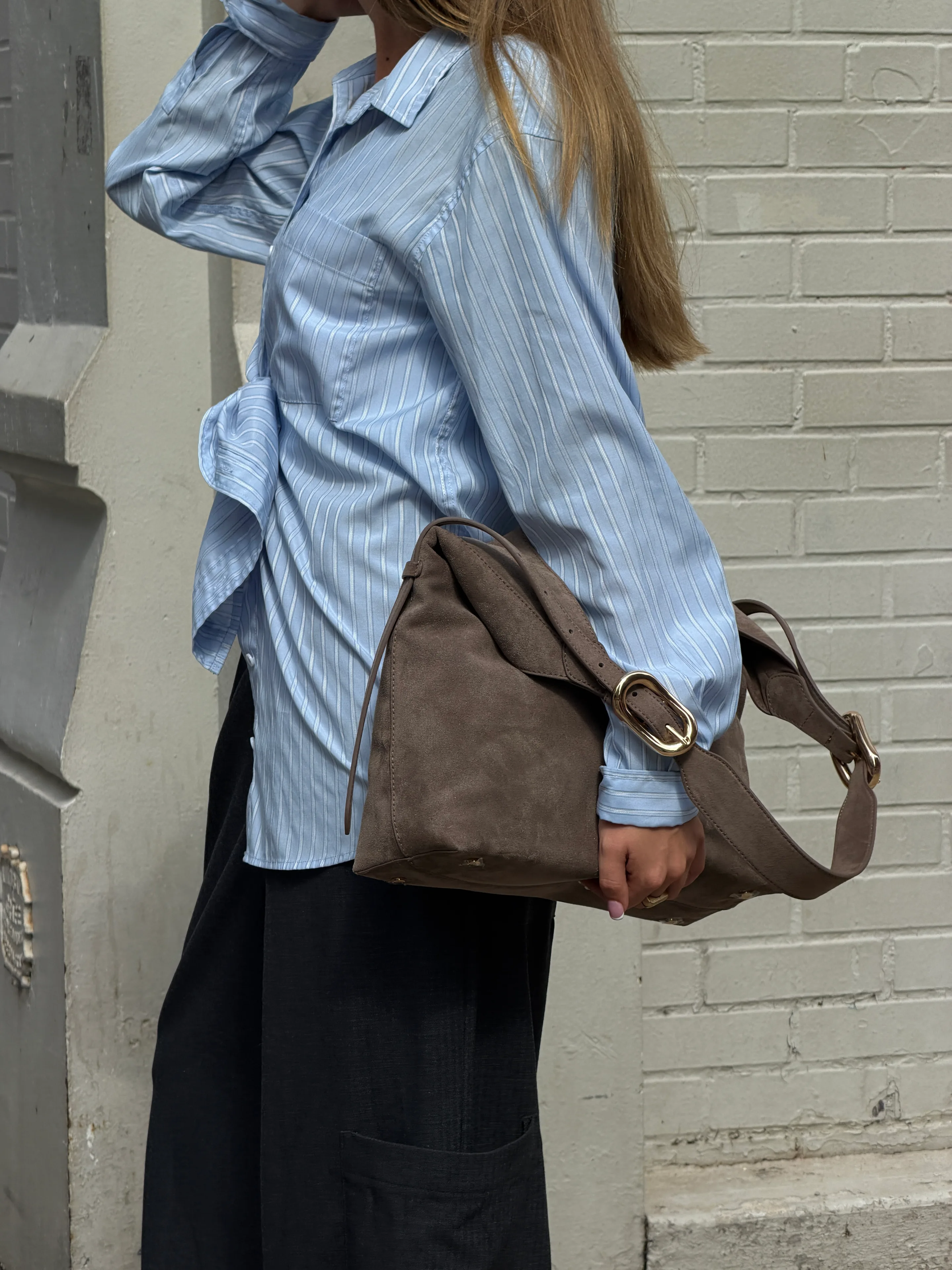 Light blue striped button-down shirt with black pants and a brown suede shoulder bag.