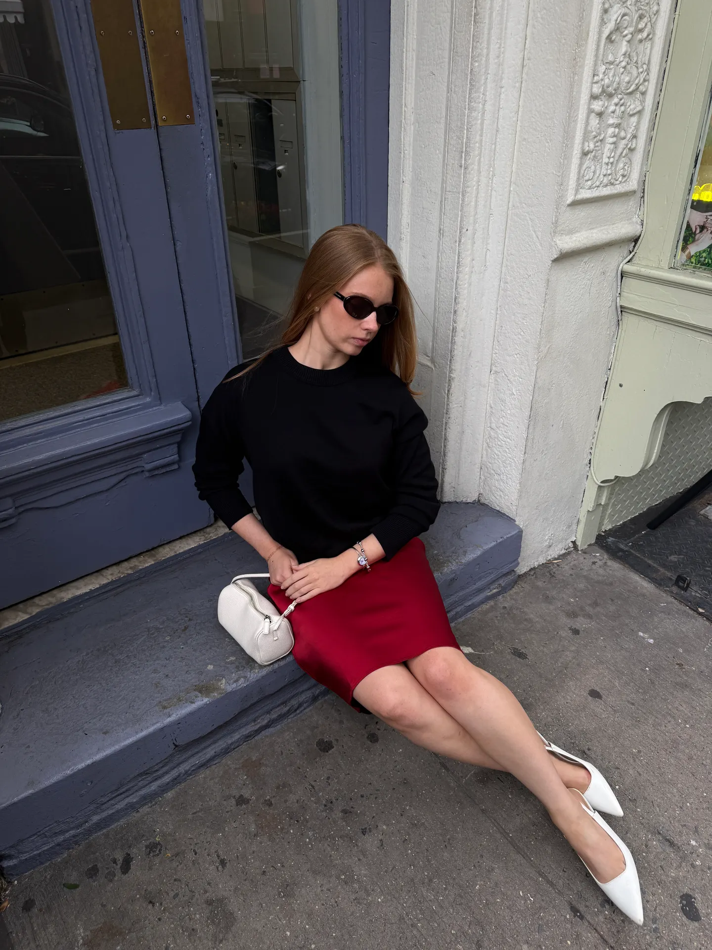 Black crewneck sweatshirt, red satin mini skirt, white handbag, white pointed-toe heels.