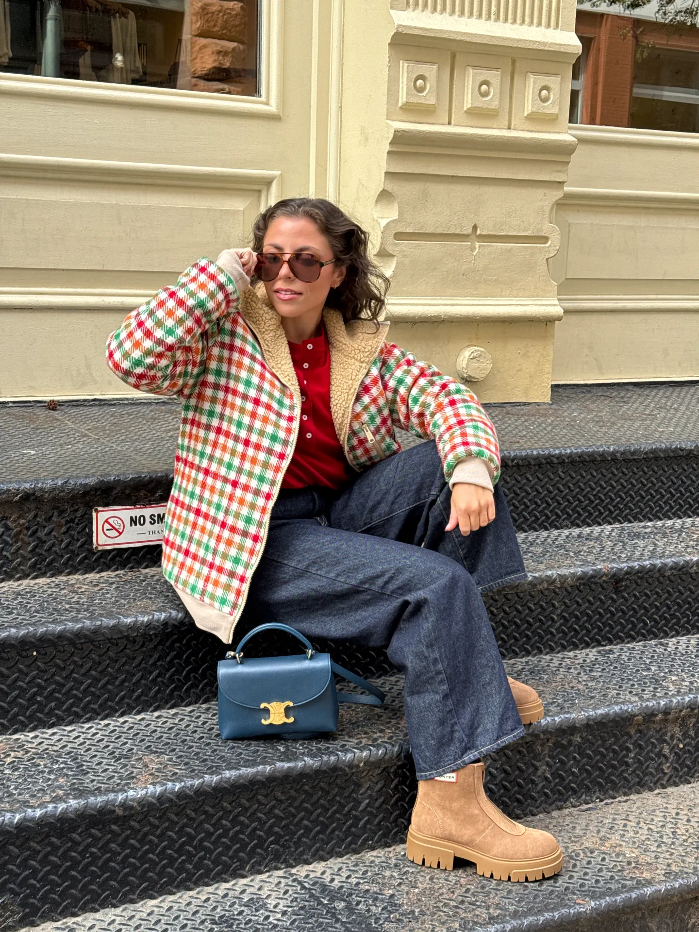 Colorful plaid fleece jacket, red top, dark wash jeans, brown boots, and blue purse.