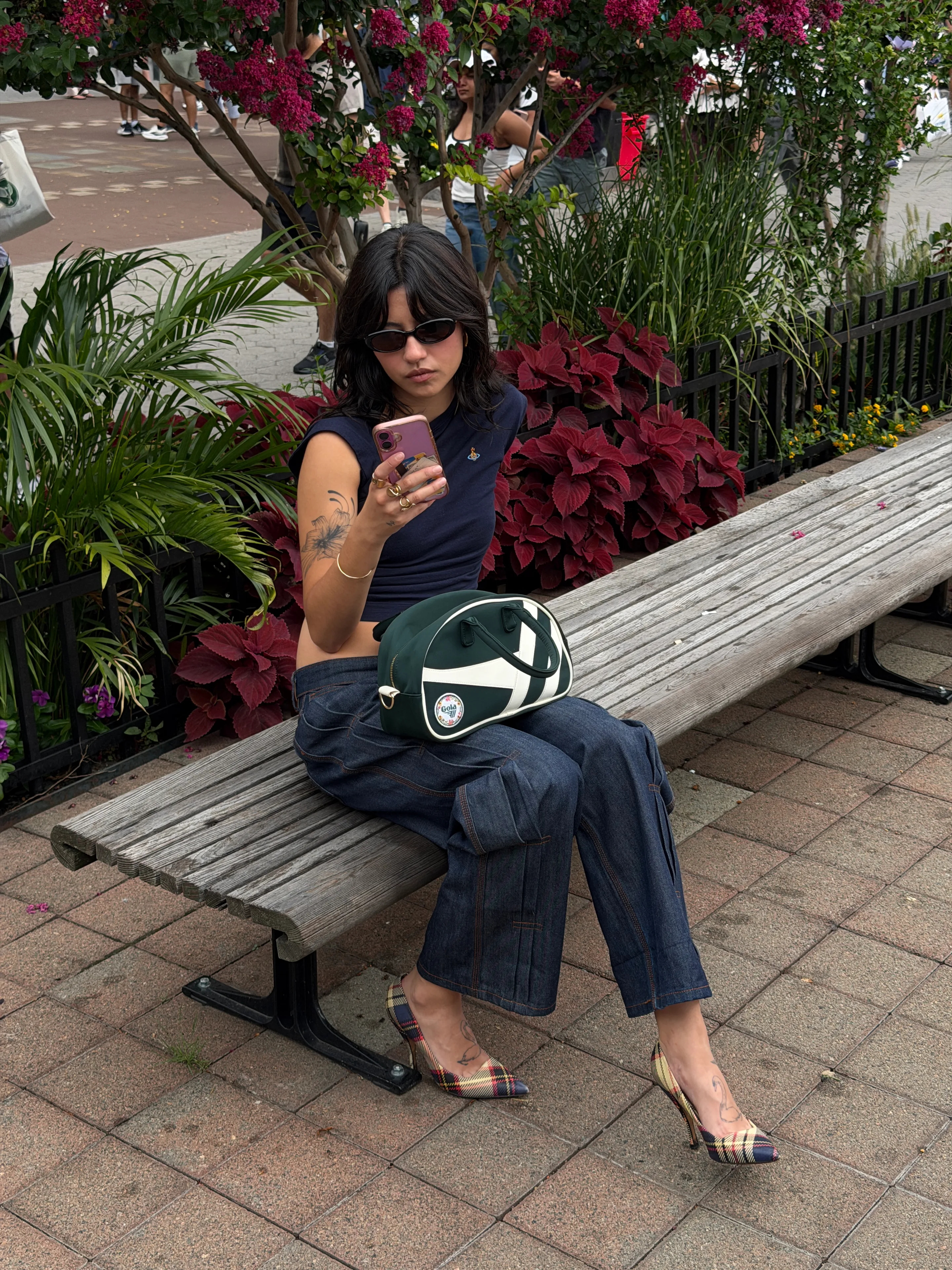 Navy crop top, dark wash wide-leg jeans, plaid heels, and green bag on a park bench.
