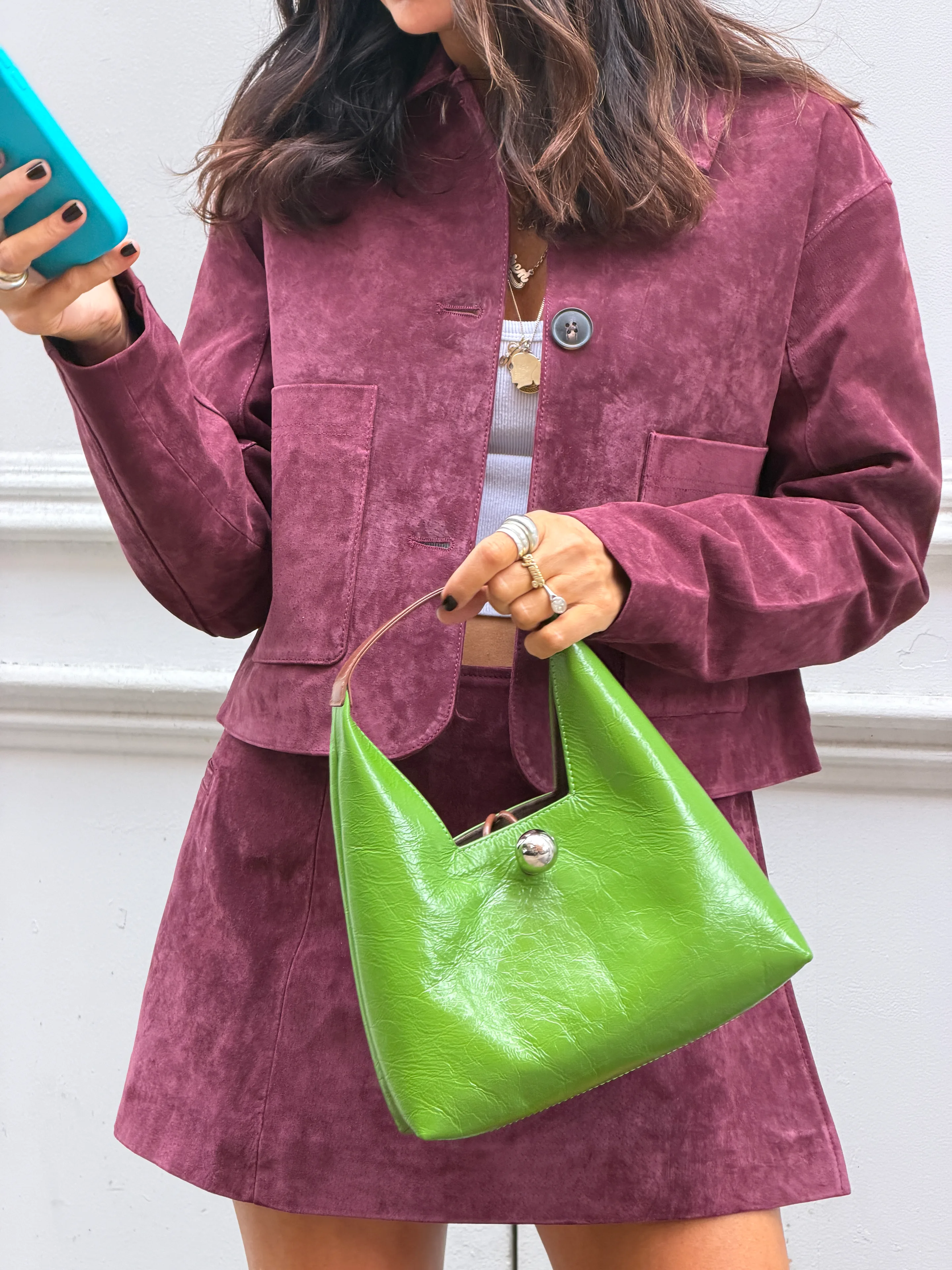 Plum suede jacket and skirt set with a bright green handbag and rings.