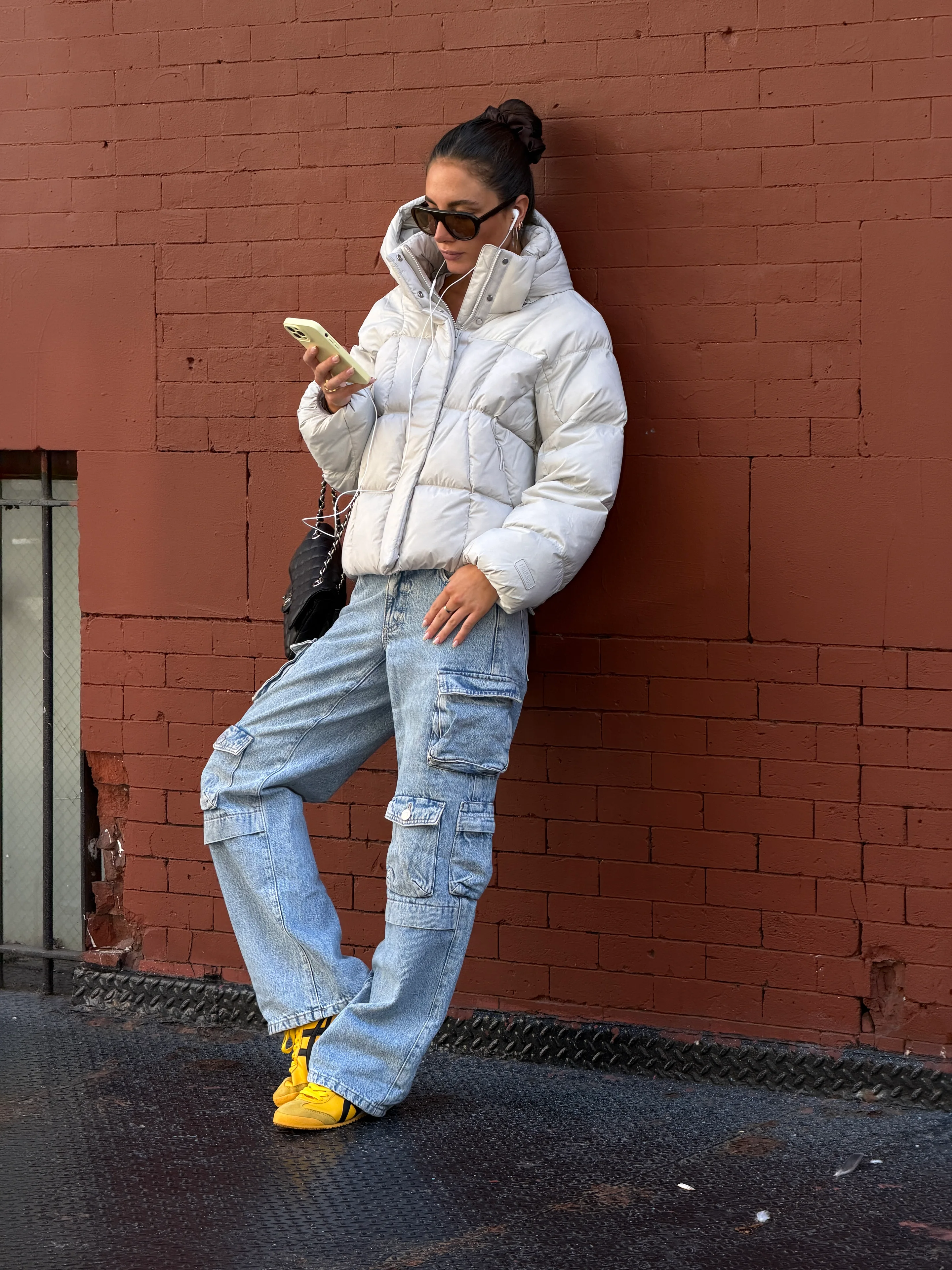 White puffer jacket, baggy cargo jeans, and yellow sneakers against a red brick wall.