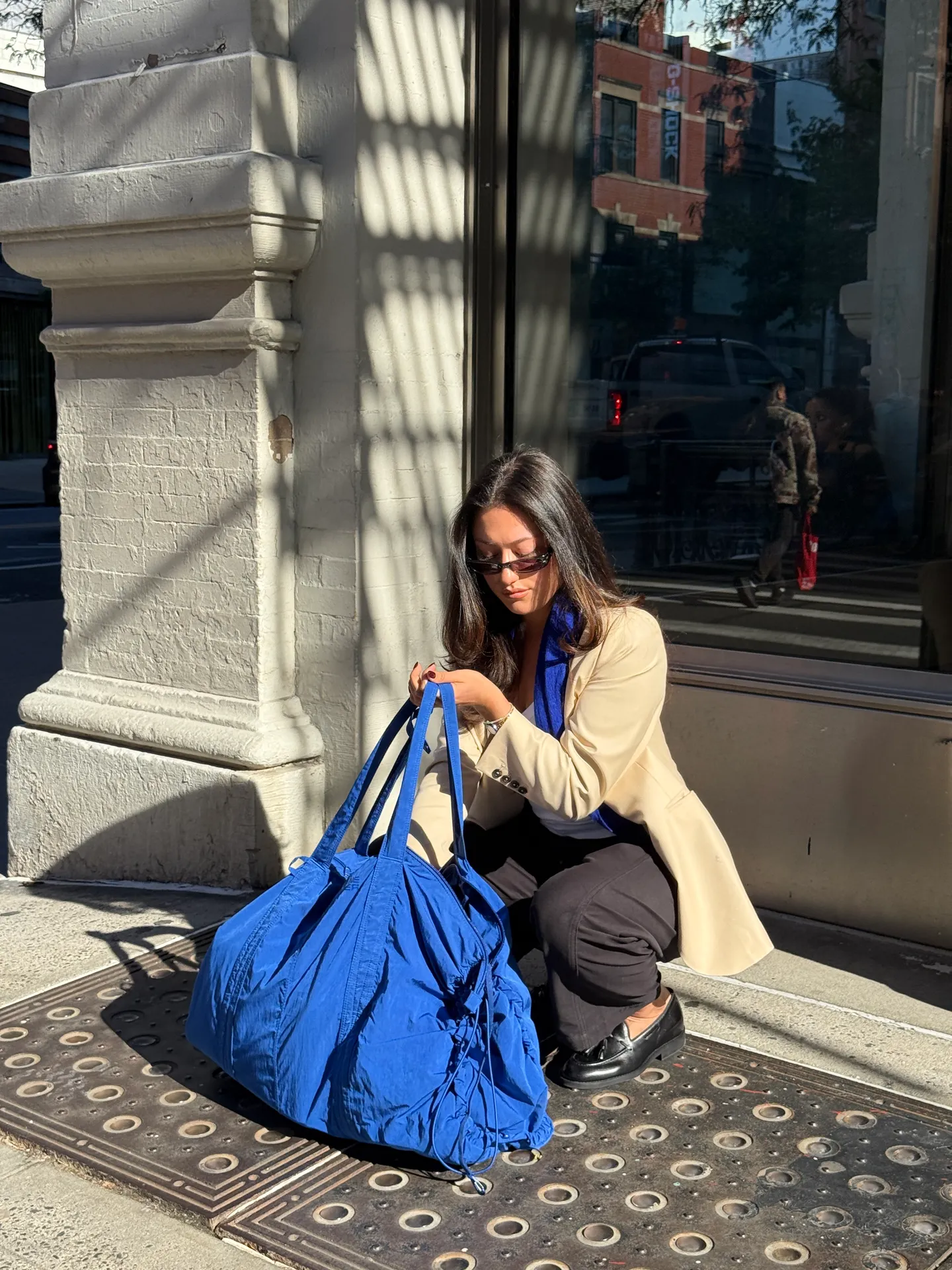 Beige blazer, black pants, black loafers, and a blue tote bag on a sunny city street.