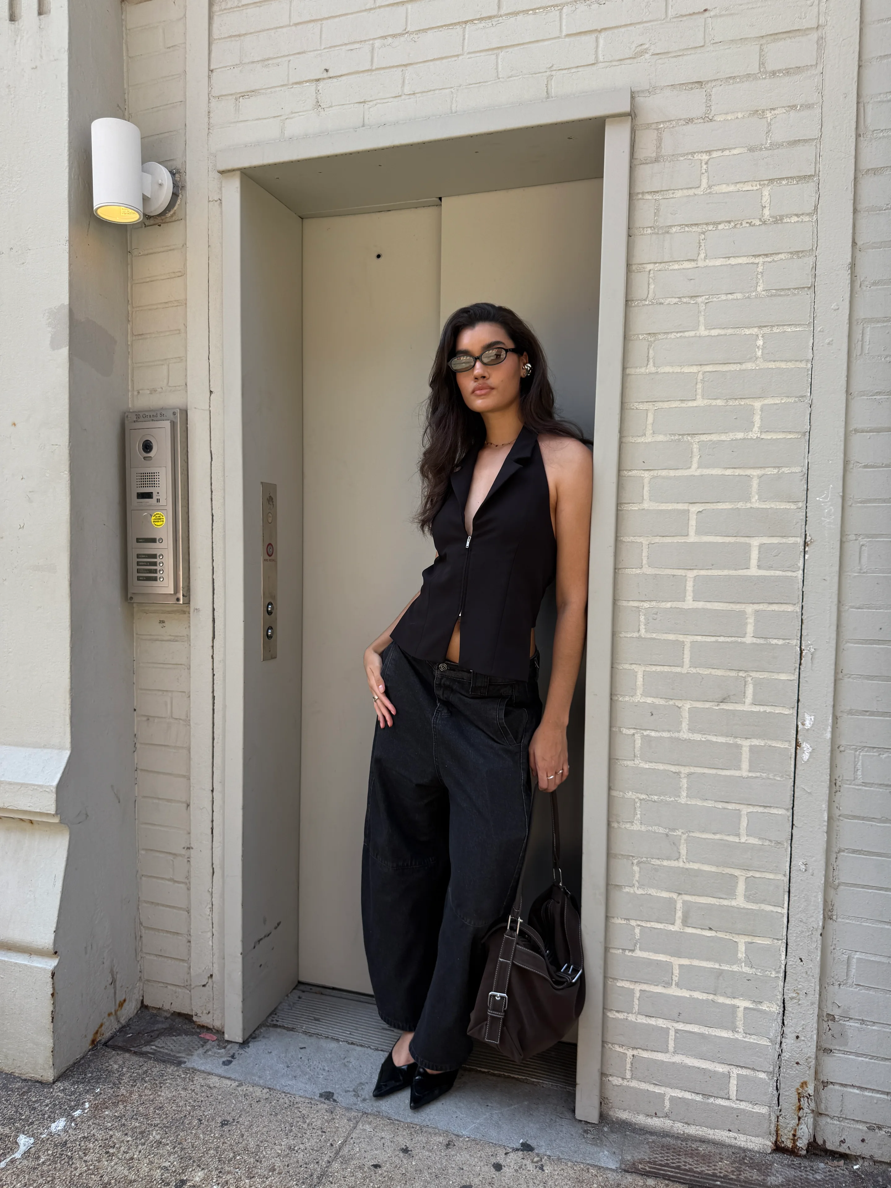 Black halter vest with dark wide-leg jeans, pointy heels, and a brown shoulder bag.