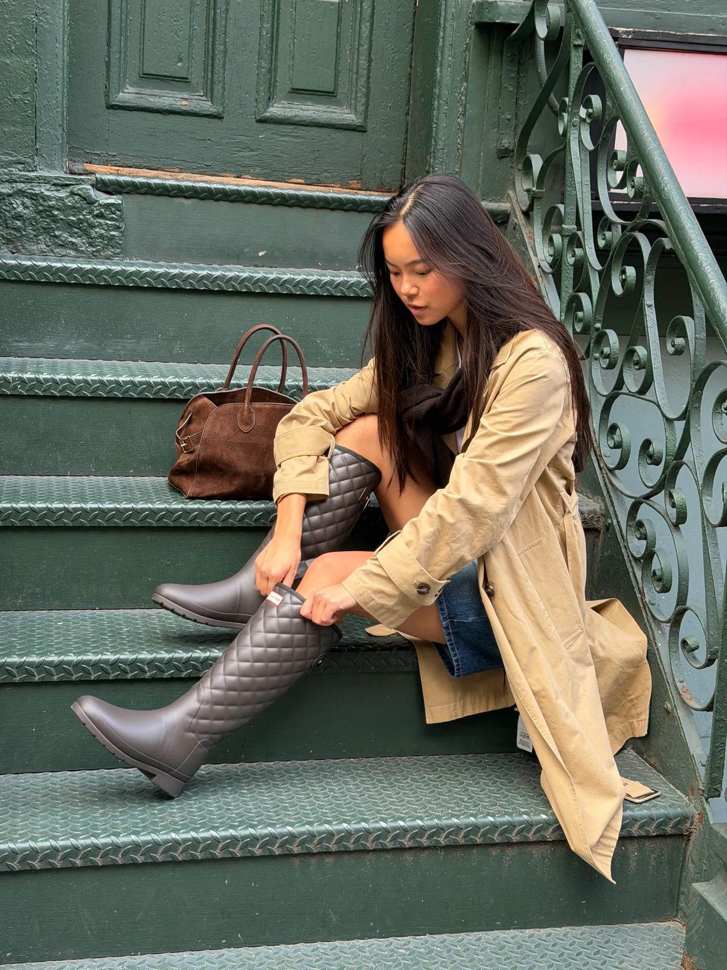 Khaki trench coat, denim shorts, and quilted gray Hunter boots on green stairs.
