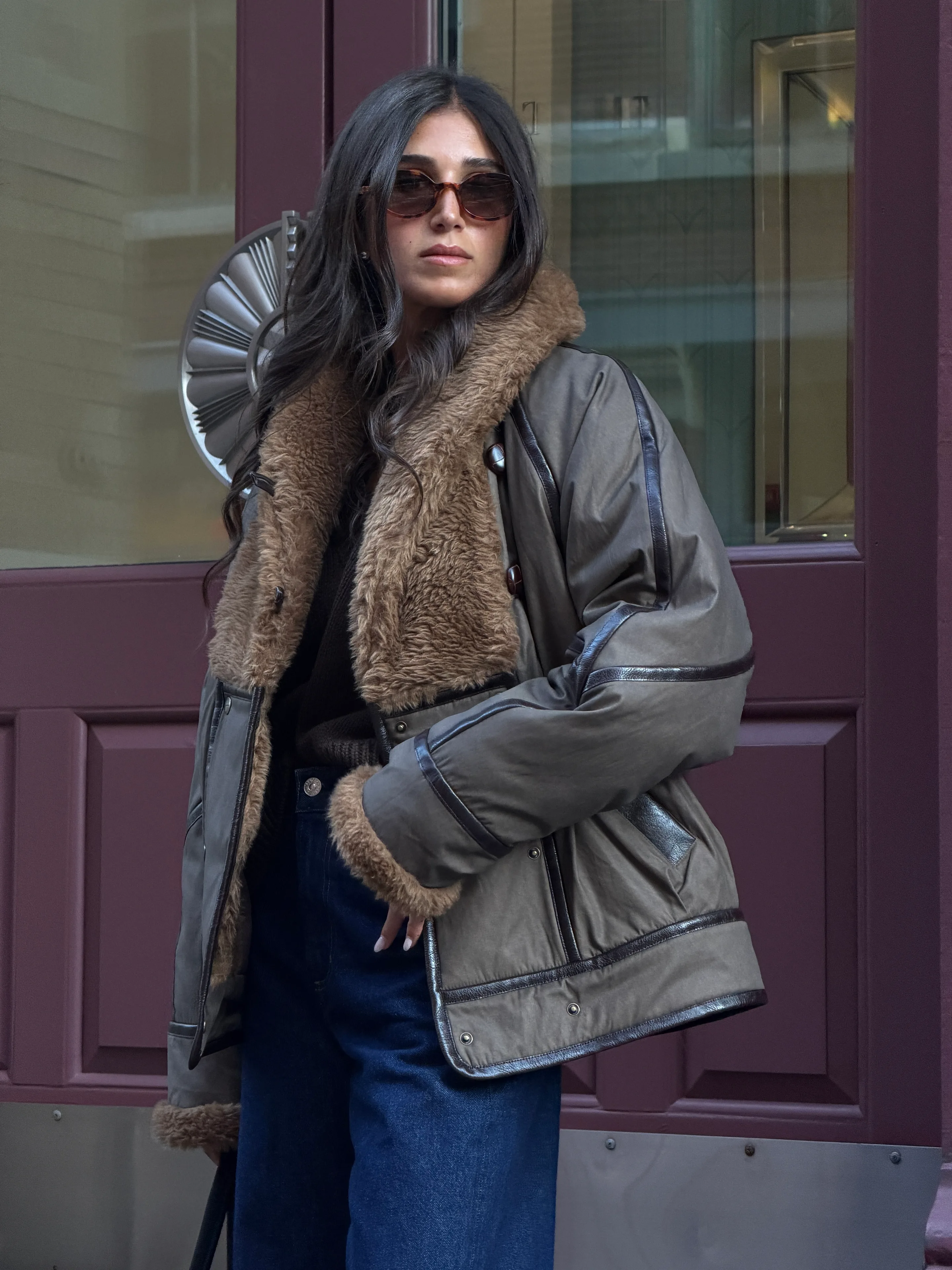 Brown shearling-lined aviator jacket, dark wash jeans, brown sunglasses.