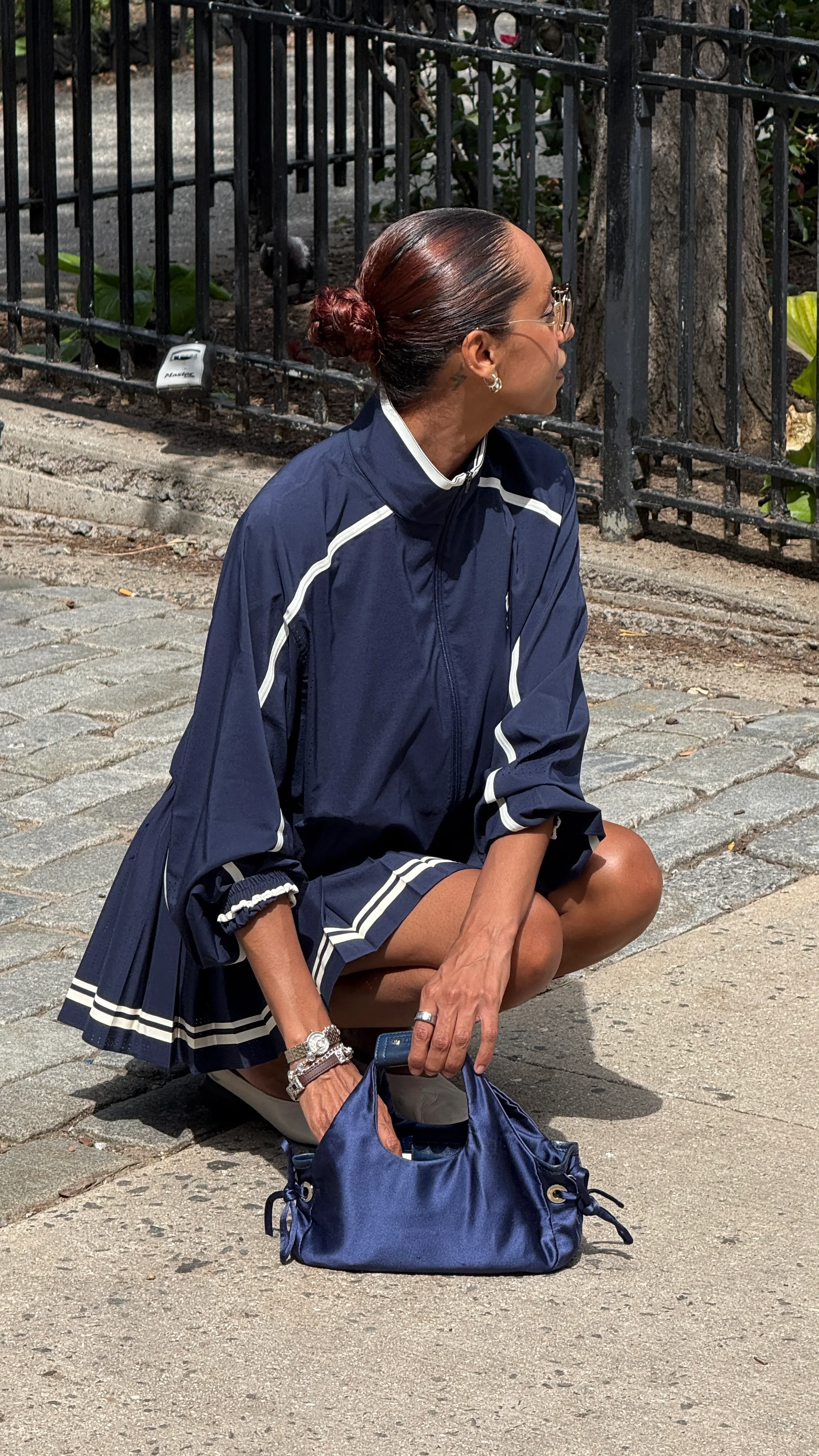 Navy track jacket and pleated mini skirt with white stripes, holding a satin purse.