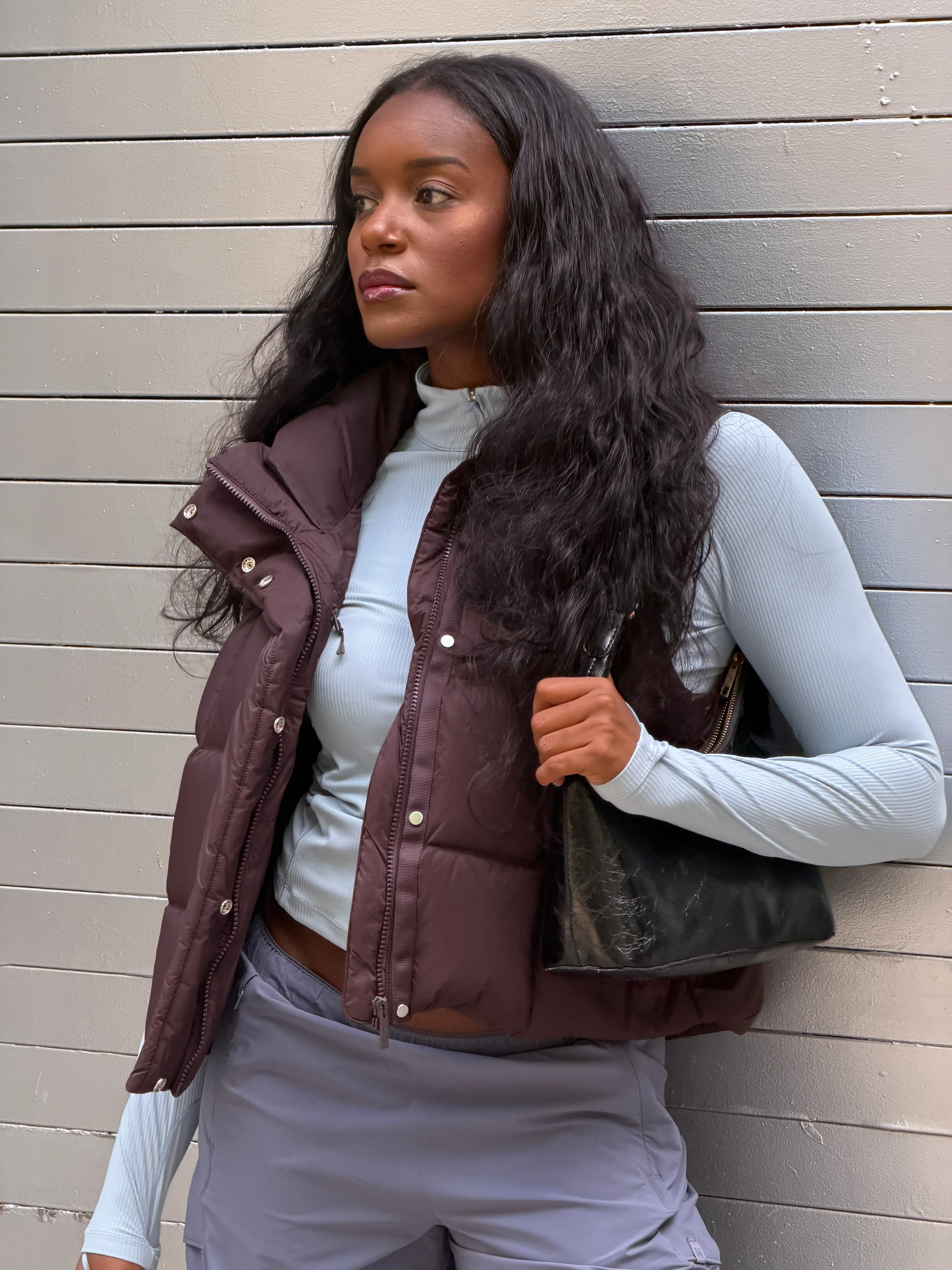 Brown puffer vest over ribbed light blue long-sleeve top and gray pants.