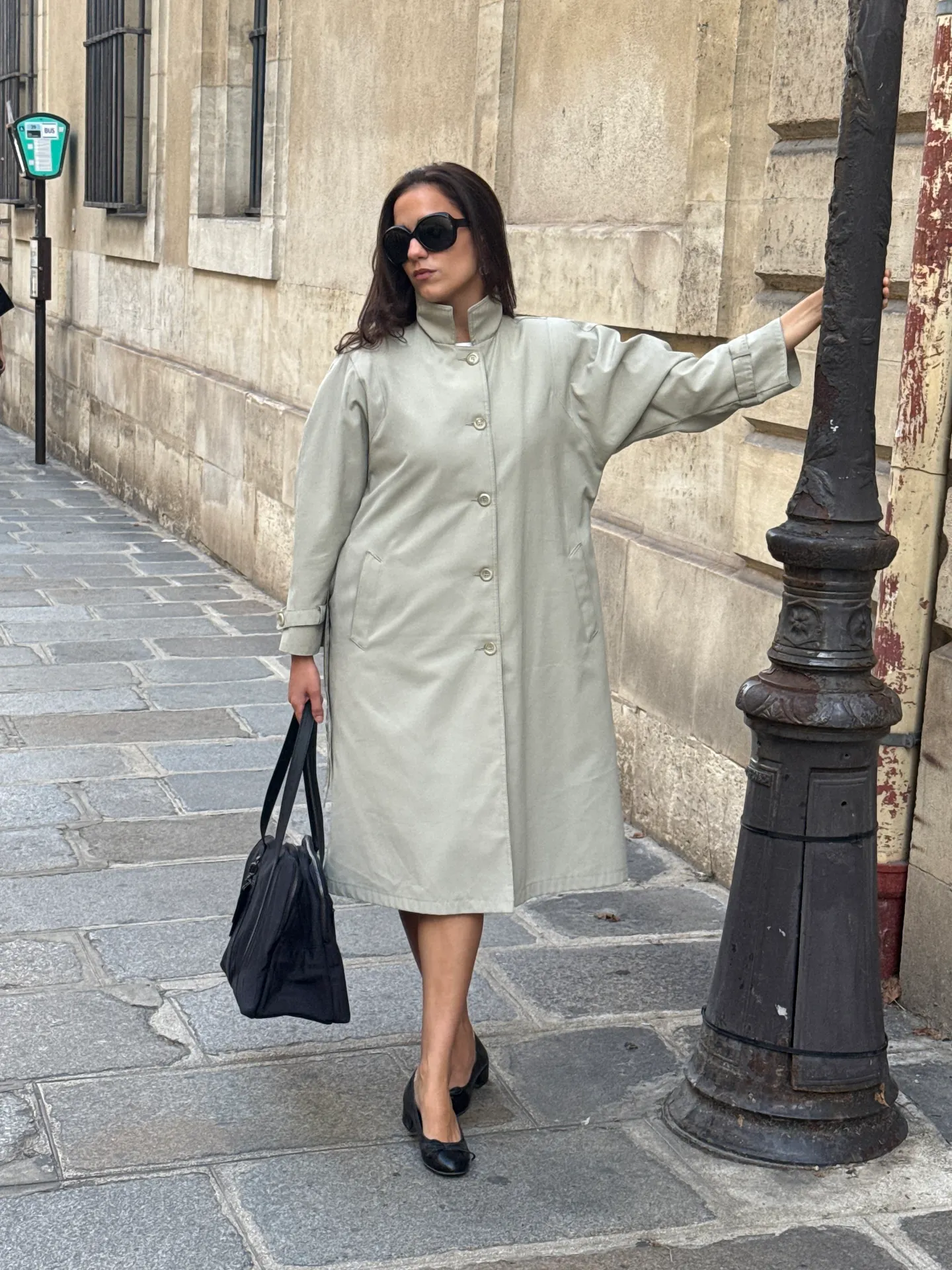 Light olive trench coat, black oversized sunglasses, black ballet flats, and a black handbag.