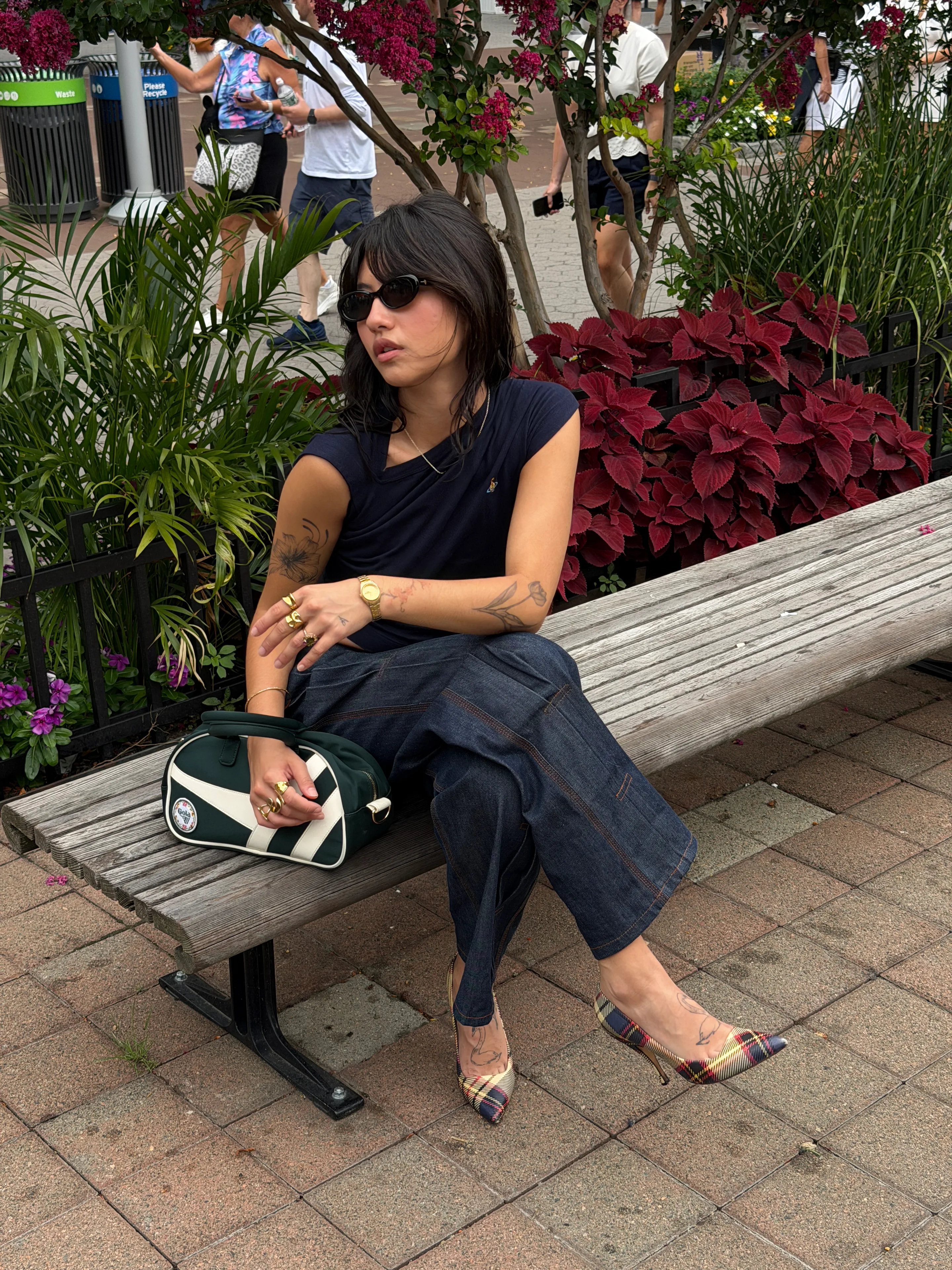 Navy asymmetrical top, dark wash jeans, plaid pumps, and green satchel.