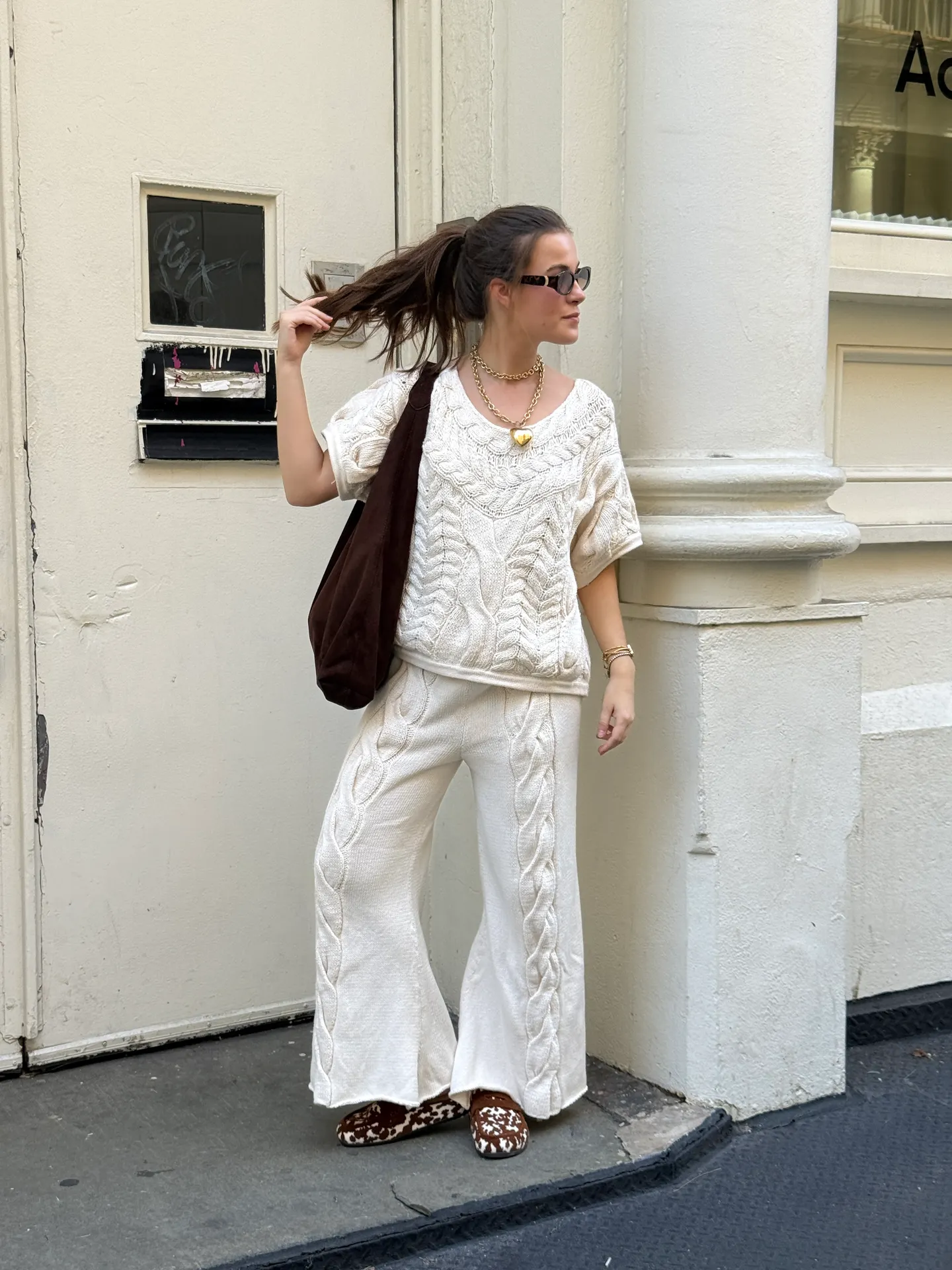 Cream cable knit top and matching wide-leg pants, brown velvet tote, and cow print loafers.