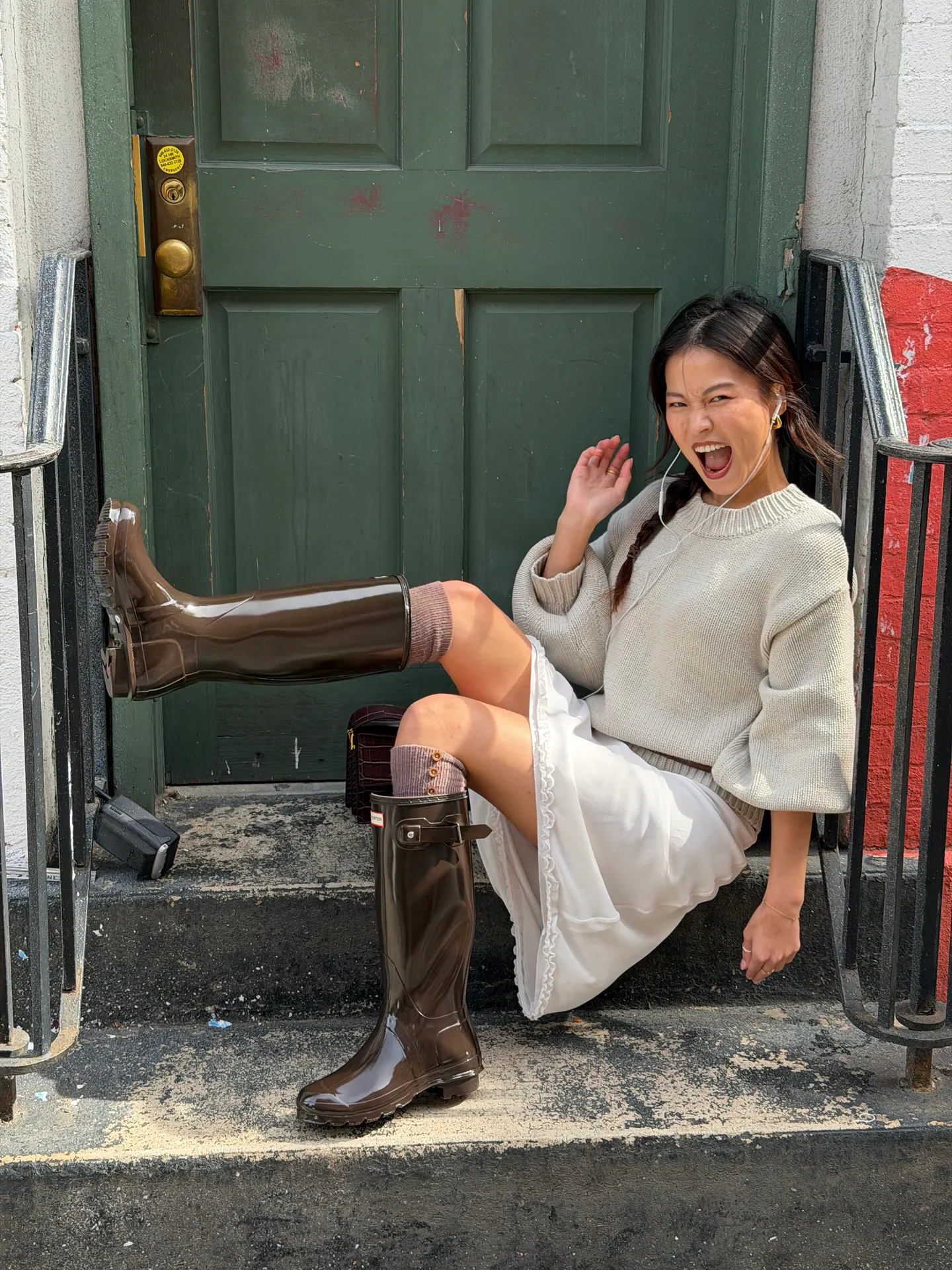 Light gray sweater, white skirt, and brown Hunter rain boots on urban steps.