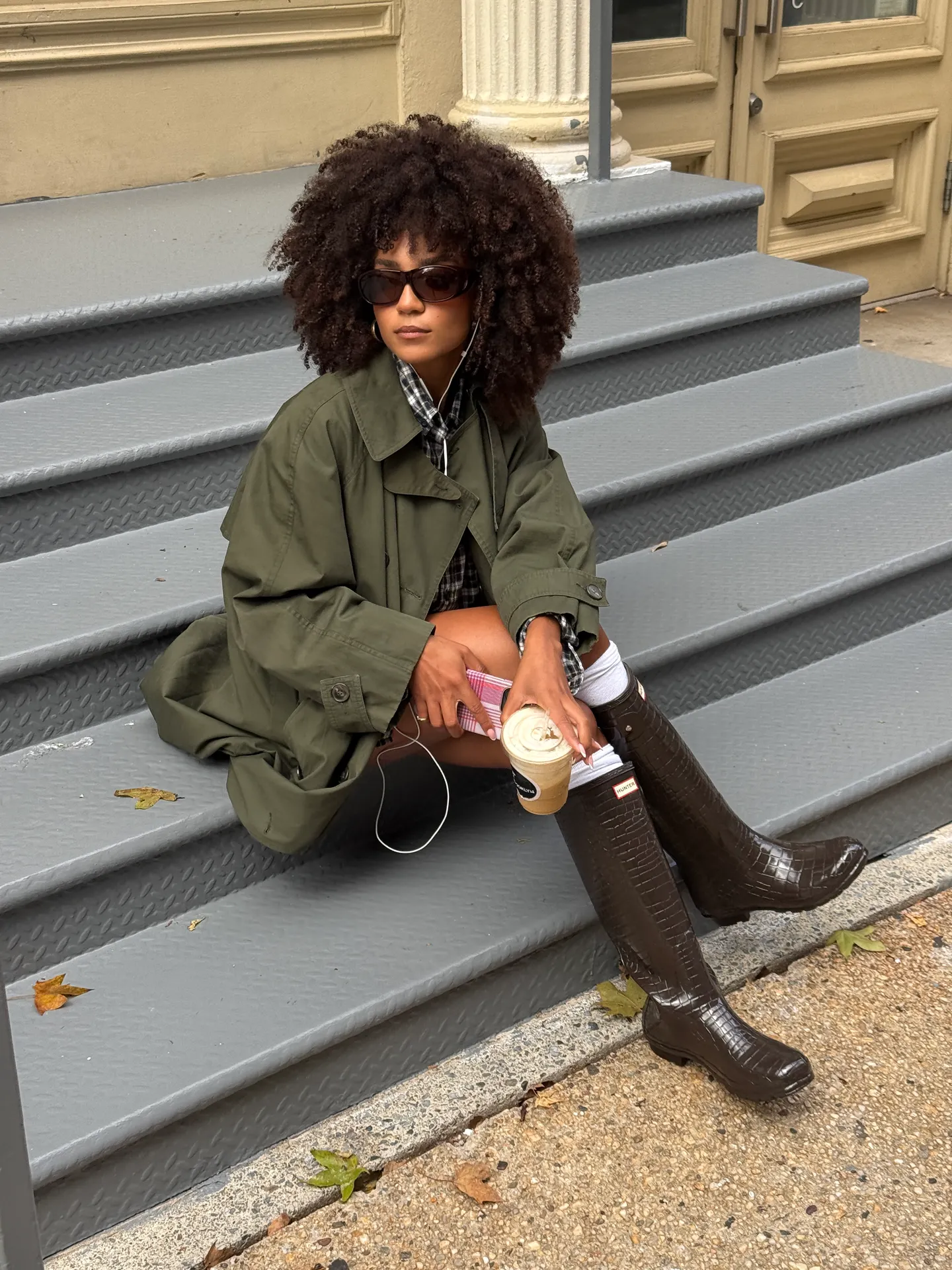 Olive trench coat, plaid shirt, and crocodile-embossed Hunter boots.