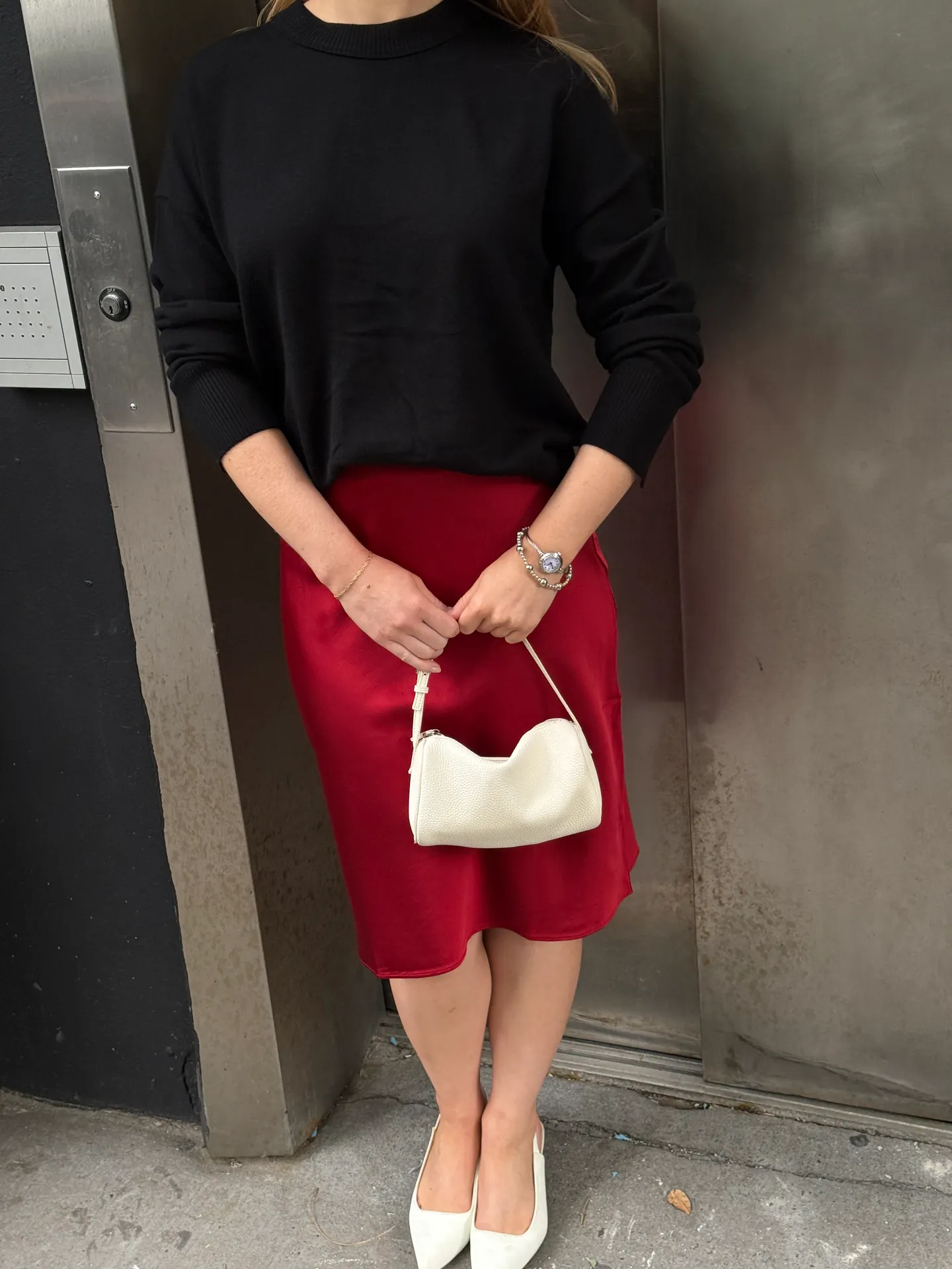 Black sweater with a red satin skirt, white slingback heels, and a white mini bag.